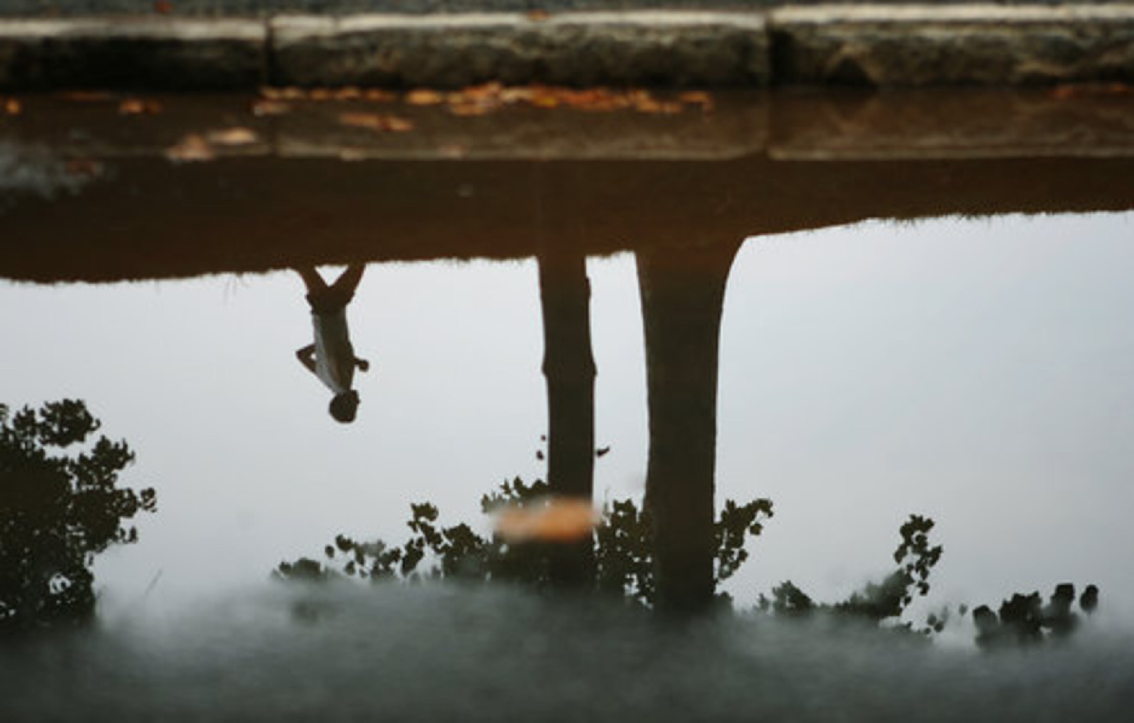 Reflected in a rain puddle, a runner jogs through Piedmont Park as the rainy weather clears up on Sunday afternoon.