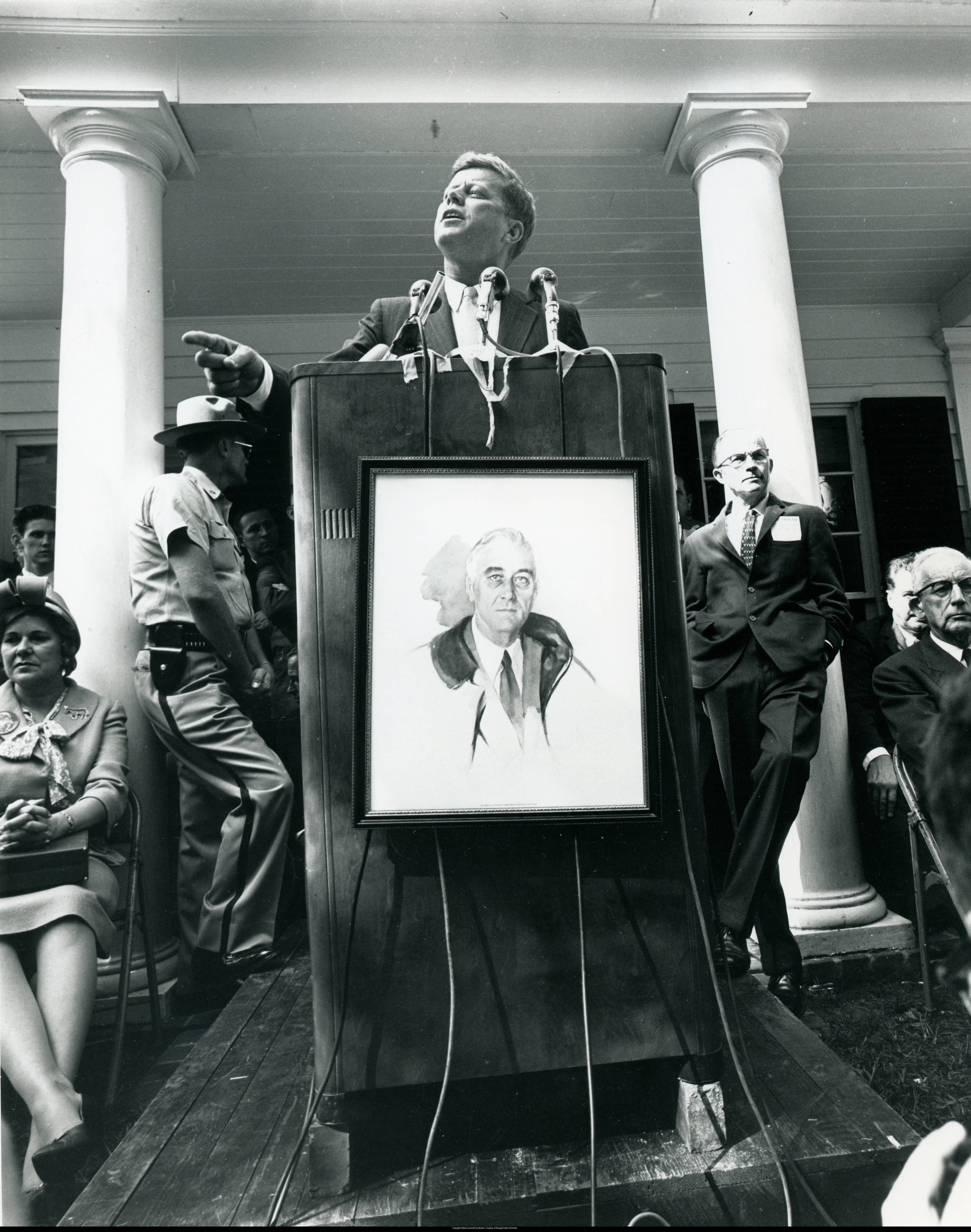 John F. Kennedy speaking at outdoor podium, Warm Springs, Georgia, October 10, 1960. Podium has copy of Elizabeth Shoumatoffs' "unfinished" portrait of Franklin Delano Roosevelt. Atlanta Journal-Constitution Photographic Archive