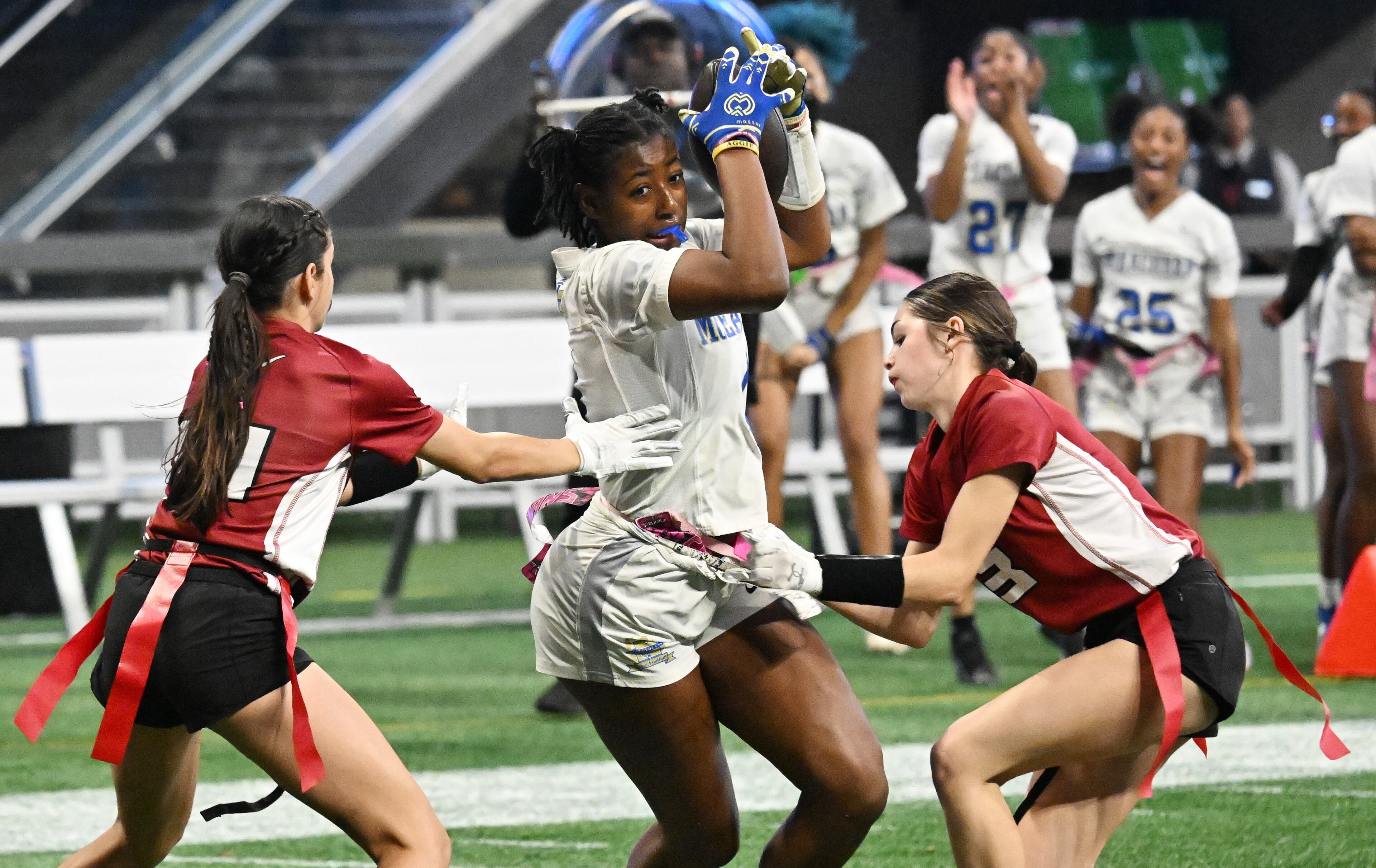 McEachern's Desirae Holley (4) drives against Lambert's Hadley Sonmez (left) and Lambert's Paige Wentworth (right) during the first half in GHSA Division 4 Flag Football State Championship game at Mercedes-Benz Stadium, Wednesday, December 18, 2024, in Atlanta. McEachern won 26-6 over Lambert. (Hyosub Shin / AJC)