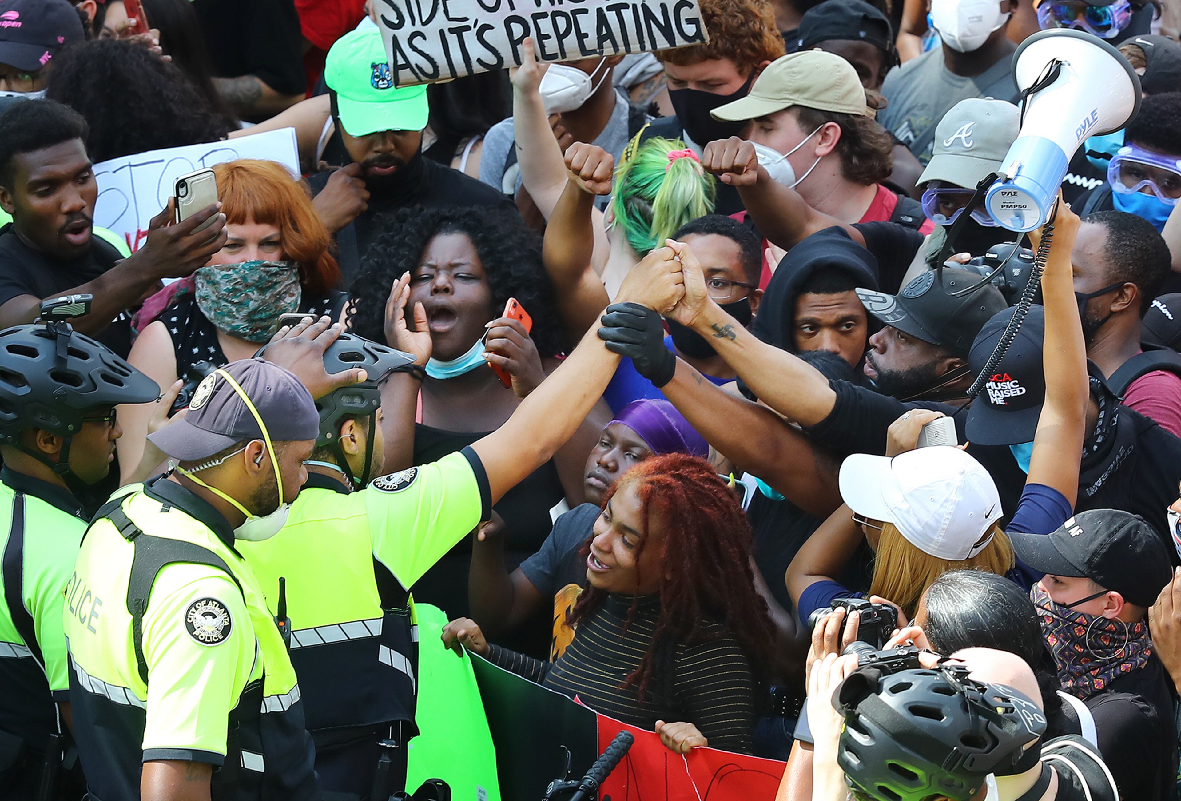 060220 Atlanta: Showing respect and solidarity an Atlanta Police officer in a bicycle unit joins hands with a protester during a street face off outside the CNN Center at Olympic Park during a fifth day of protests over the death of George Floyd on Tuesday, June 2, 2020, in Atlanta. Curtis Compton ccompton@ajc.com