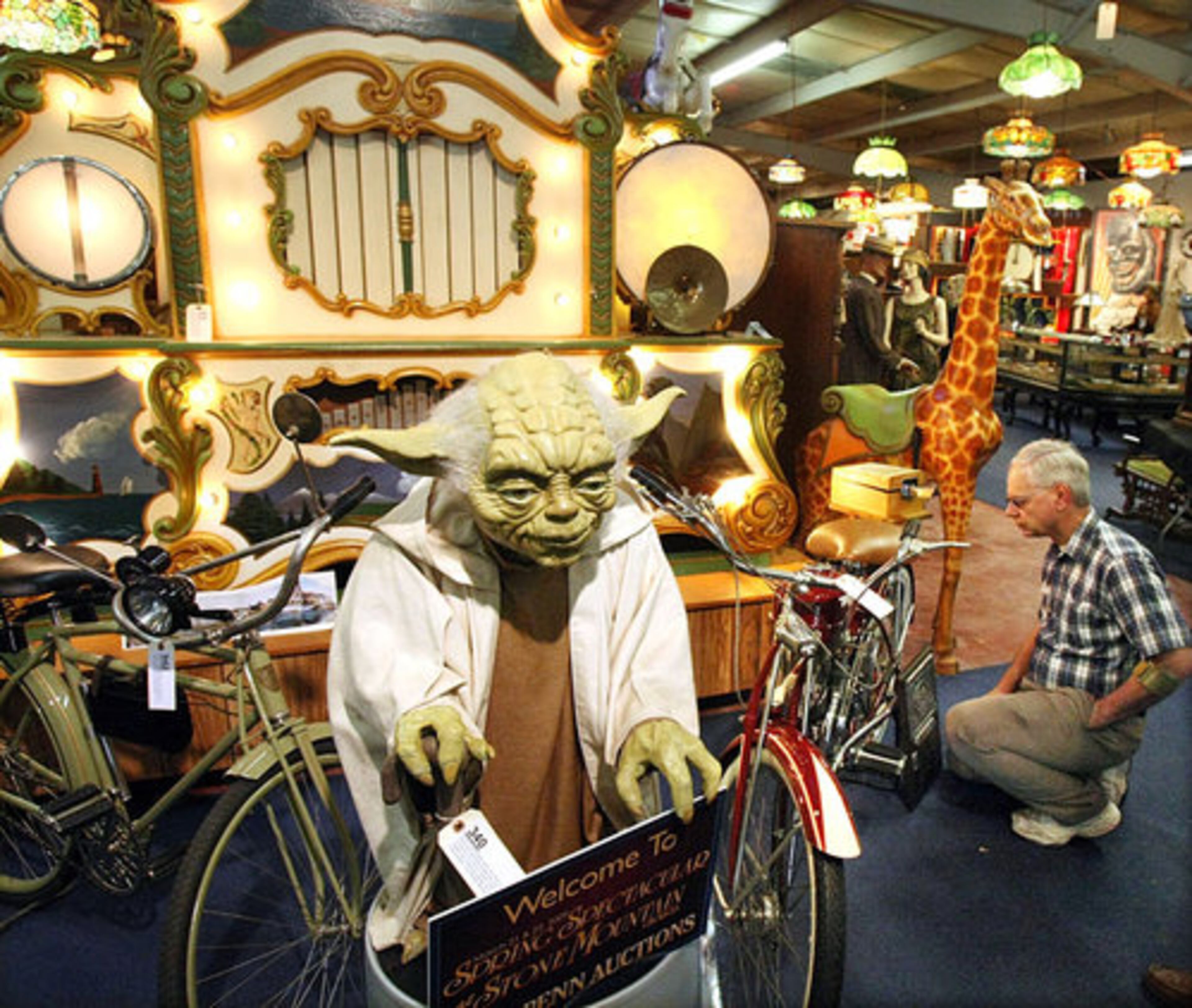 On Saturday, Bobby Protsman saw a lifetime of collectible begin to disappear. The owner of the recently closed Stone Mountain Antique Car and Treasure Museum began auctioning his collection. Here, Rick Fasnacht, of Cumming, looks over a 1950 Whizzer Bicycle while a movie theater display figure of Yoda from 'Star Wars' looms.