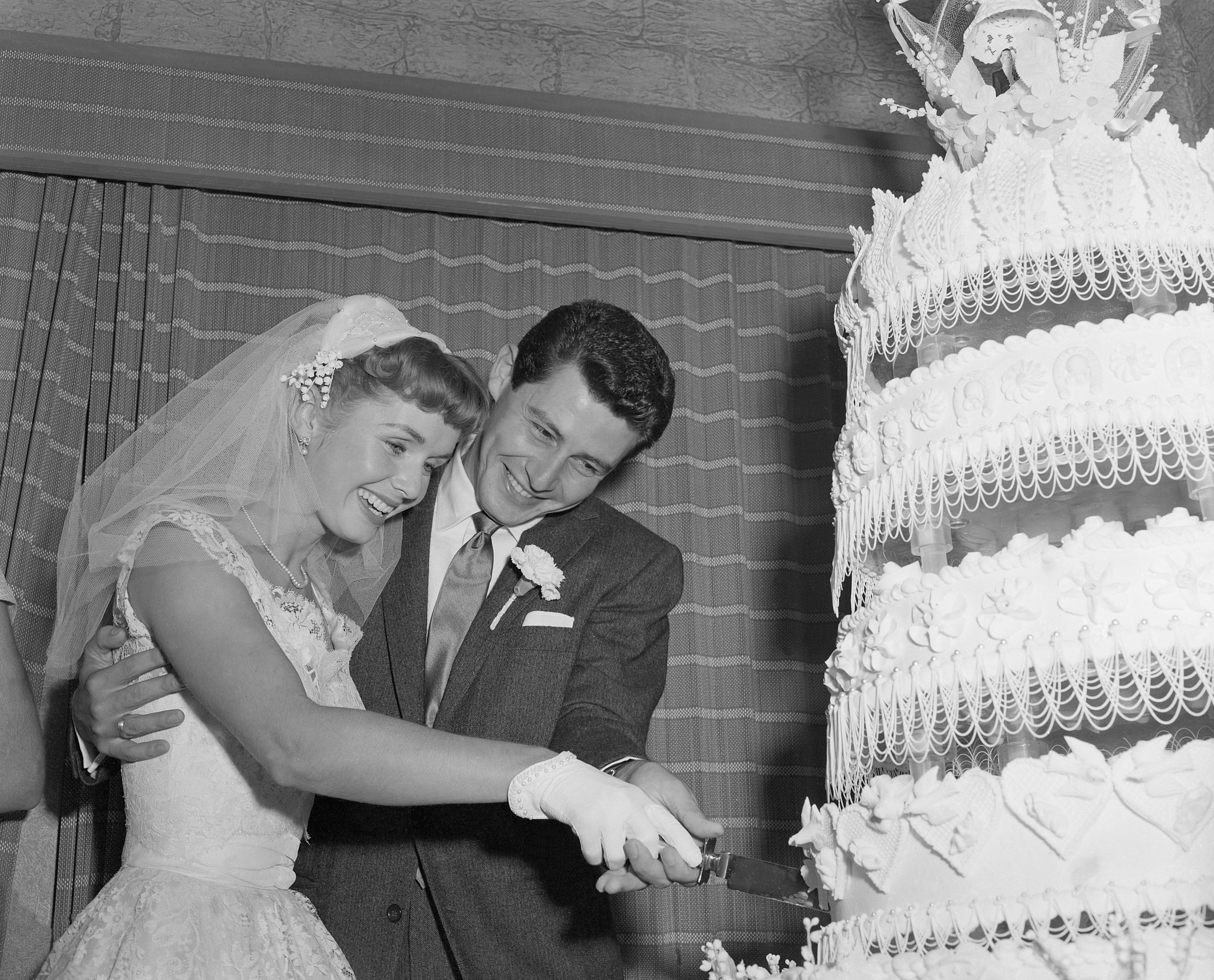 Actress Debbie Reynolds and singer Eddie Fisher cut their towering wedding cake after they were married at Liberty, N.Y., in 1955. (Photo by Bettmann / Contributor / Getty Images)