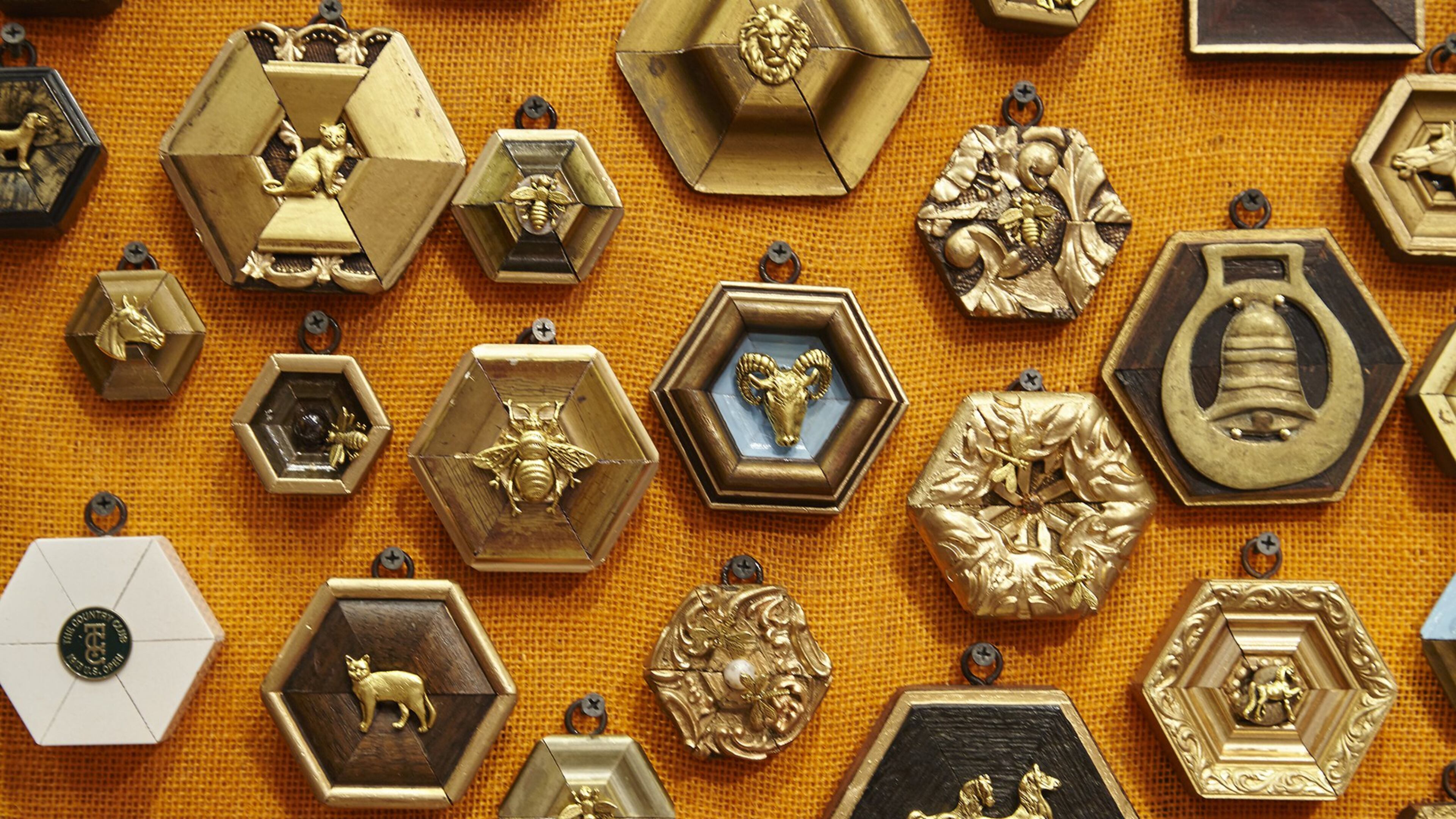 A collection of gold and wooden Museum Bees by Trace Mayer is nailed to an orange canvas. They are antique frames that are re-cut and a ornament such as a gilded bee is placed in the center. CONTRIBUTED BY Emily Followill Photography