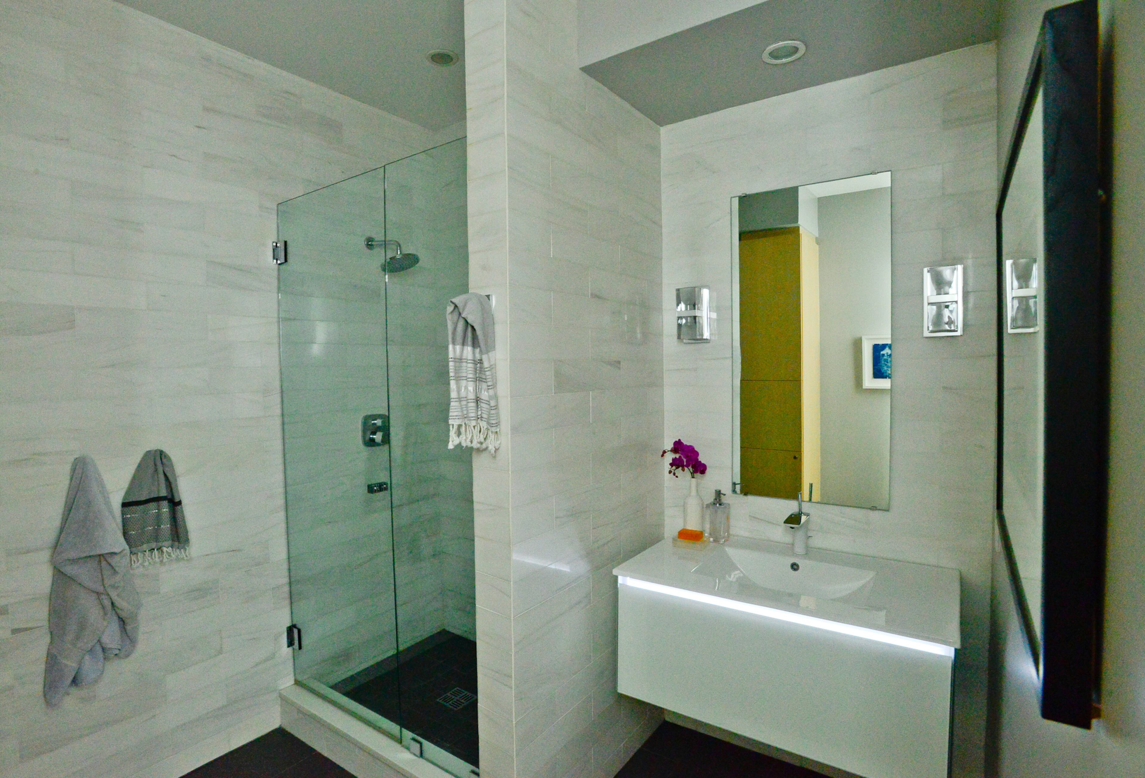 Both bathrooms were gutted and renovated in a contemporary style. The wall tiles are Bianco Dolomiti marble, through Stone Source in New York. The white glass Robern vanity with LED lighting was purchased through European Sink in Atlanta. Fixtures are Hansgrohe and Newport Brass.