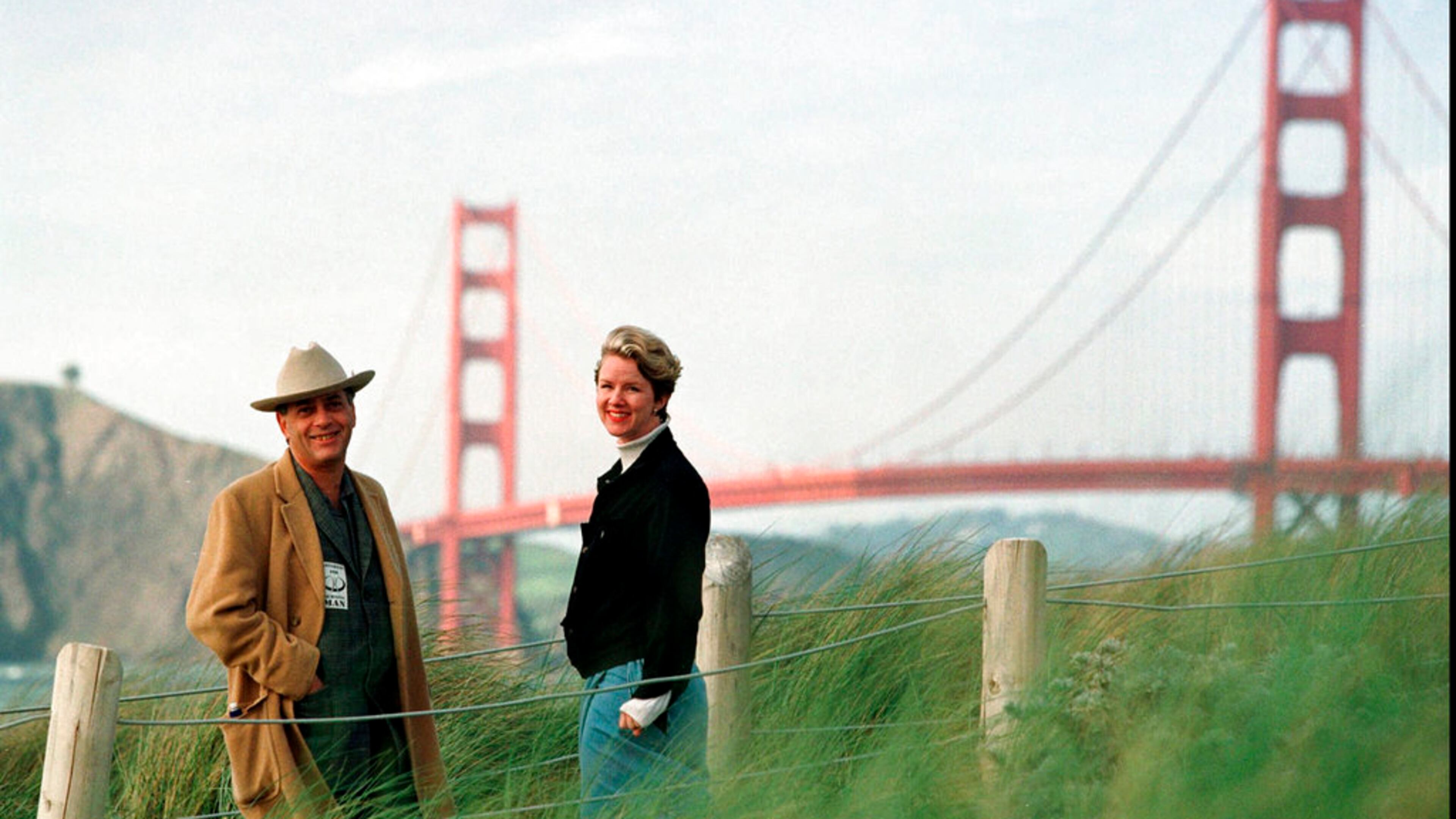FILE - In this March 30, 1998, file photo, Larry Harvey, left, and Marian Goodell, two of the founders of the Burning Man festival walk near Baker Beach in San Francisco with the Golden Gate Bridge in the background. Harvey, the co-founder of the "Burning Man" festival has died. He was 70. Burning Man Project CEO Marian Goodell says Harvey died Saturday, April 28, 2018, morning at a hospital in San Francisco. The cause was not immediately known but he had suffered a stroke on April 4. Harvey created Burning Man on a San Francisco beach in 1986, later moving the annual event to Nevada's Black Rock Desert. (AP Photo/Eric Risberg, File)