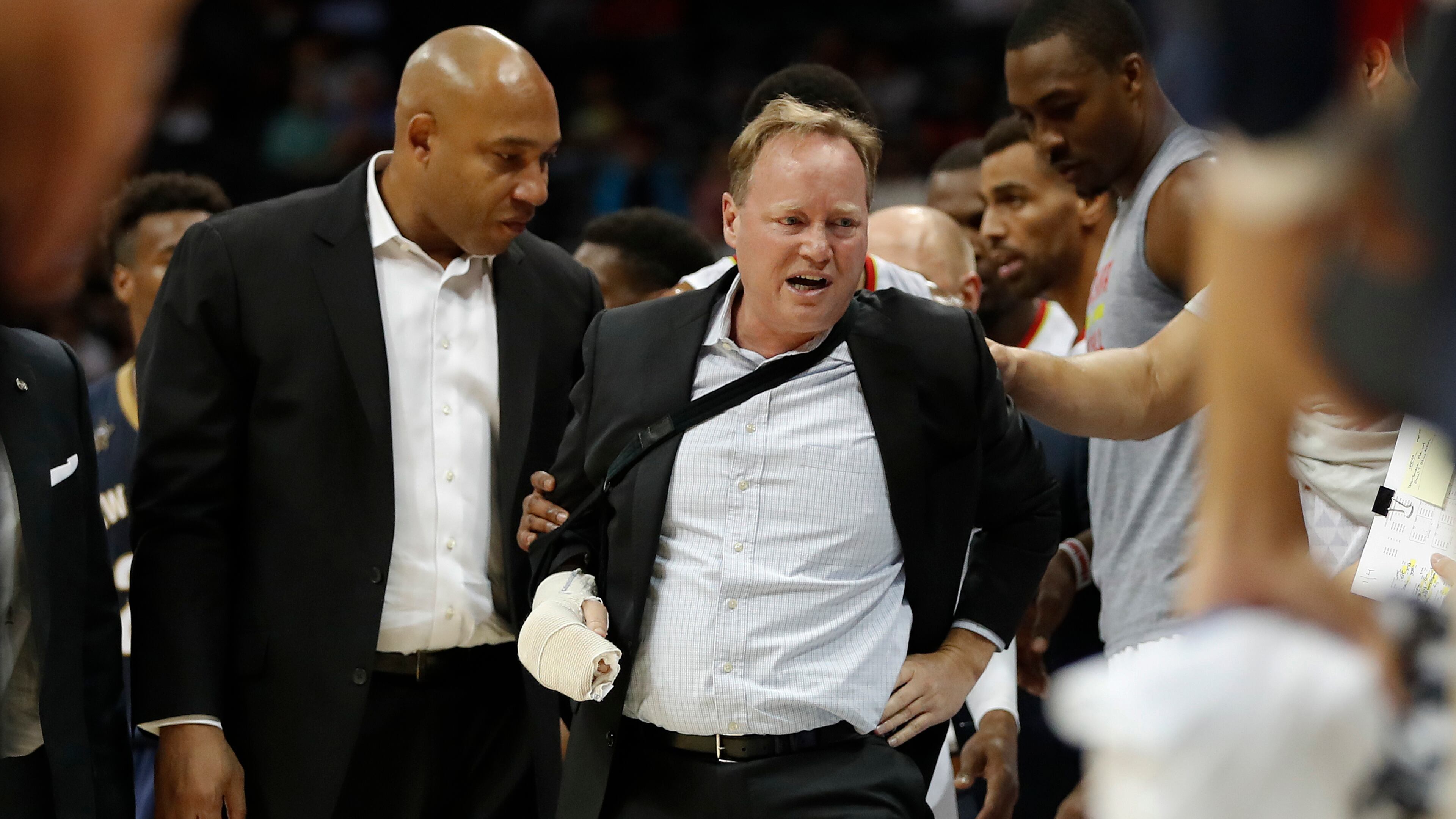Atlanta Hawks coach Mike Budenholzer (center) is helped to his feet by assistant coach Darvin Ham (left) after he was run over along the sideline during the first half of the team's preseason game against the New Orleans Pelicans Tuesday, Oct. 18, 2016, in Atlanta. Budenholzer, who was already nursing an injured hand, left the game.