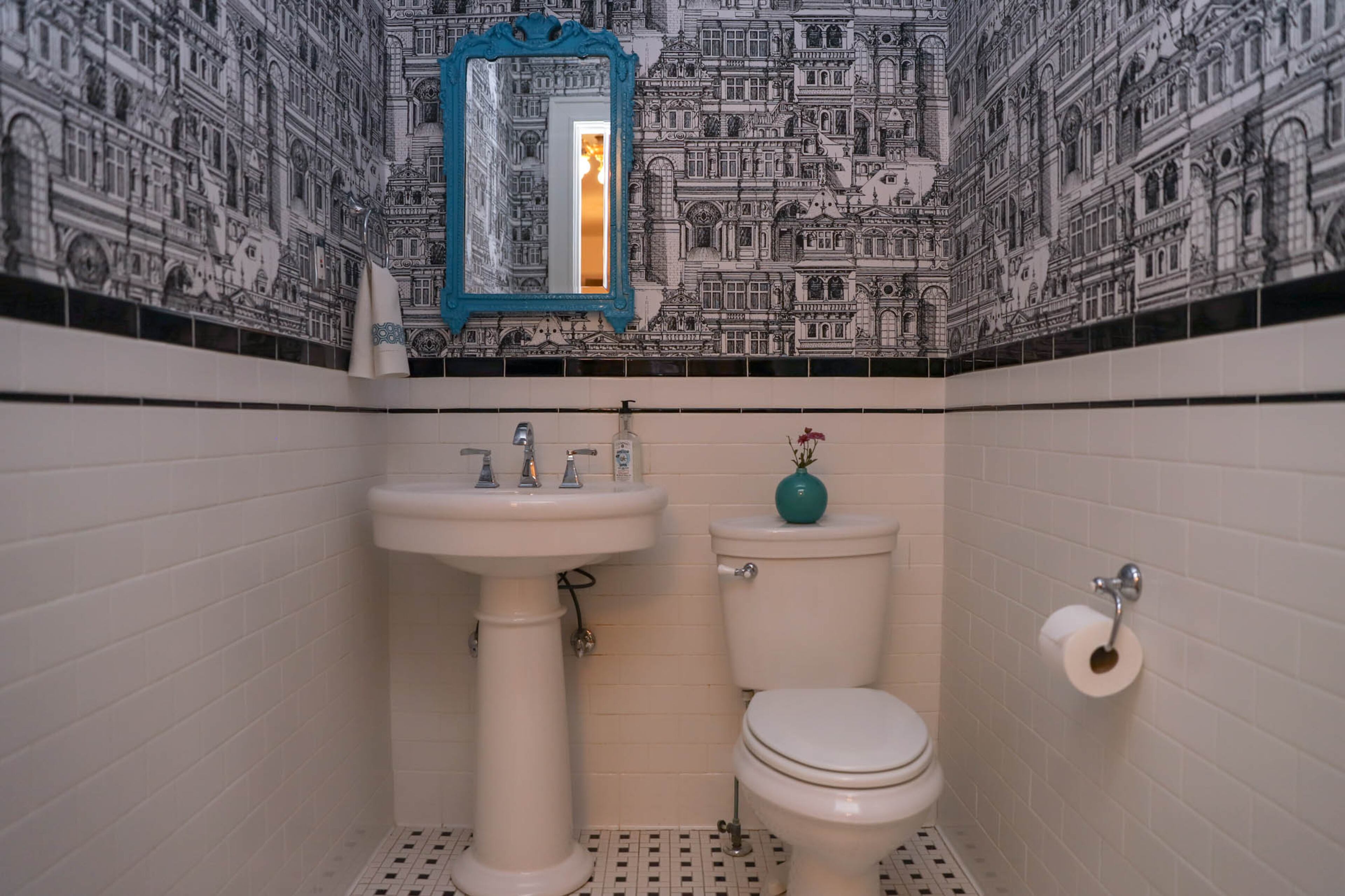 The daunting task of decorating high walls was eased by Brittney Gove's willingness to using wallpaper. The architectural black-and-white design in the powder room makes a statement, while a pop of bright blue from the mirror adds a fun focal point.