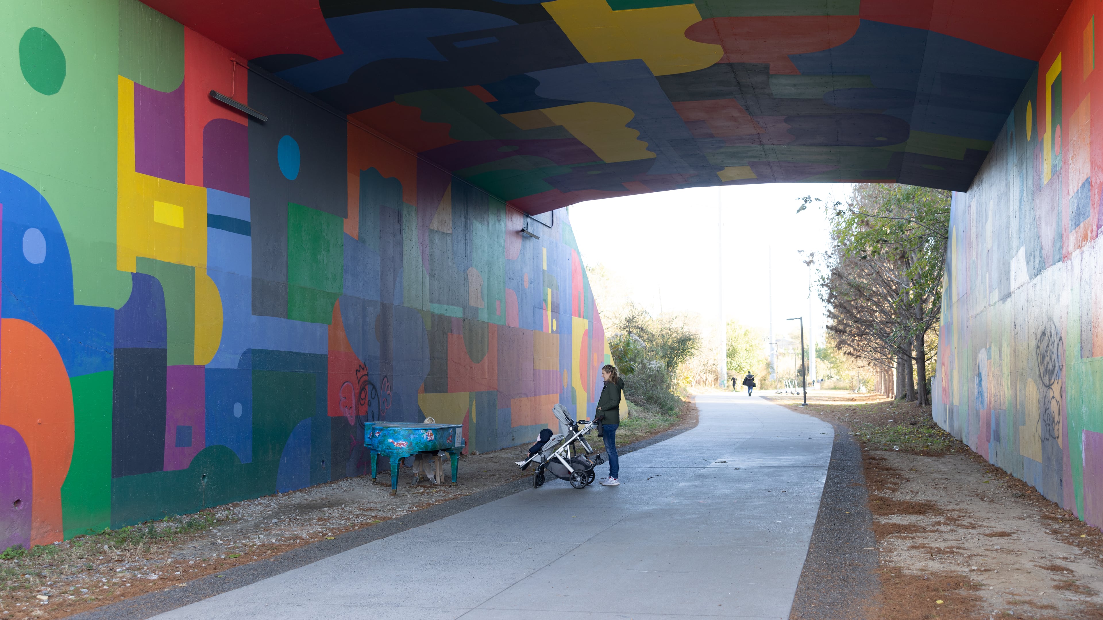 Woman walking baby in stroller and admiring piano at Beltline Northeast Trail on November 21, 2022