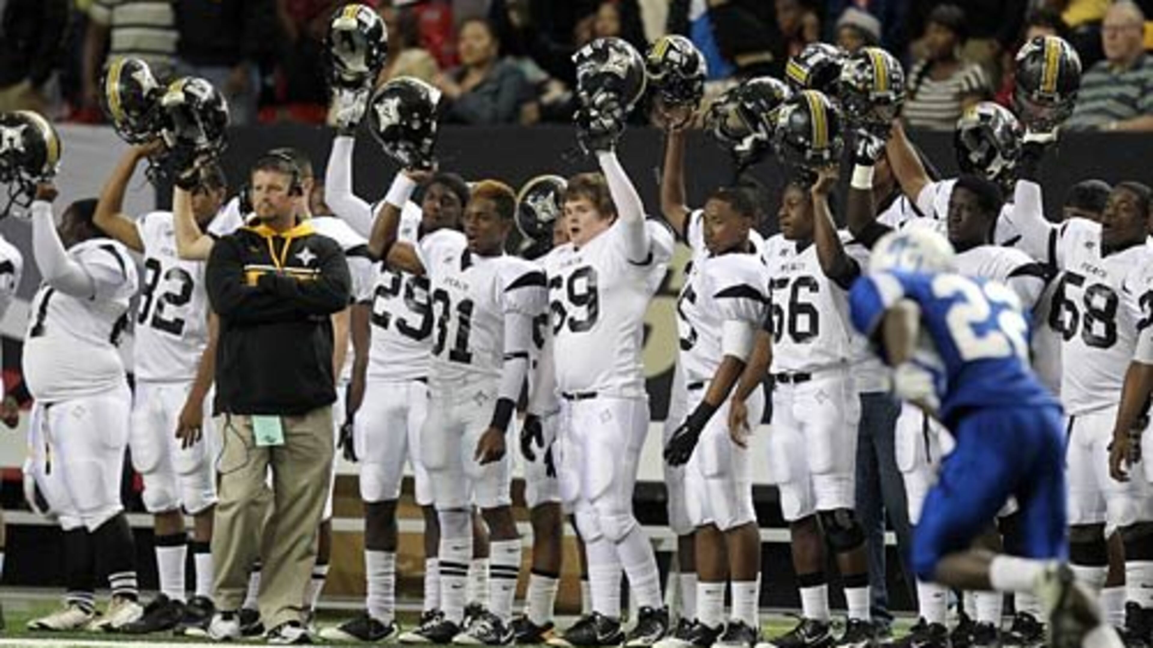 Peach County coach Chad Campbell, left, watches the opening kickoff as players raise their helmets on the sideline to start the Class AAA title game.