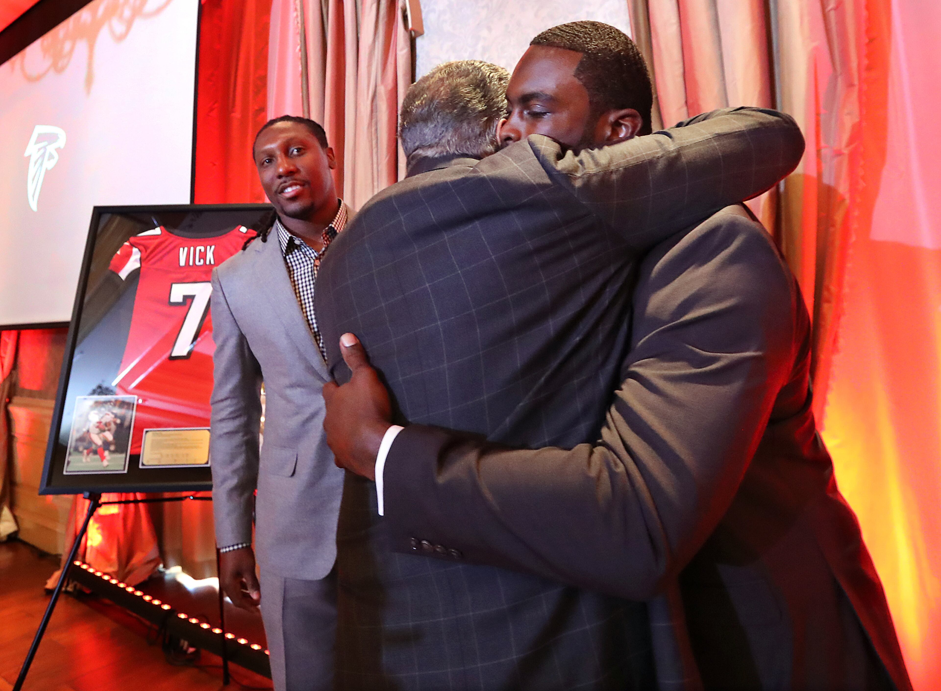 Former Falcons quarterback Michael Vick hugs owner Arthur Blank with former Falcons wide reciever Roddy White looking on as the franchise honored Vick and White as they officially retire from the NFL on Monday, June 12, 2017, in Atlanta.