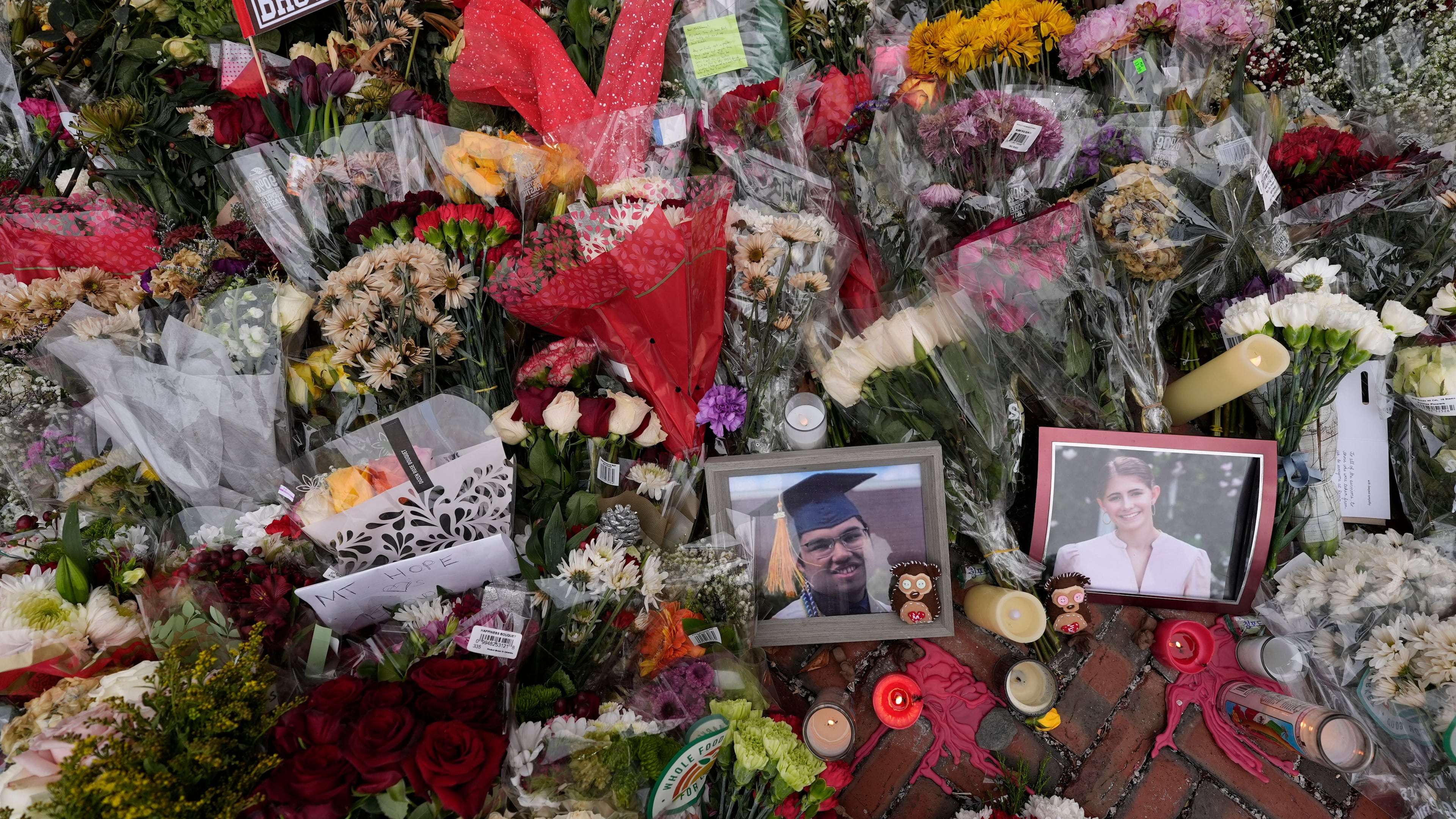 FILE - Photos of Brown University shooting victims Mukhammad Aziz Umurzokov, left, and Ella Cook, are seen amongst flowers at a makeshift memorial at the school's Van Wickle Gate, Dec. 17, 2025, in Providence, R.I. (AP Photo/Robert F. Bukaty, File)