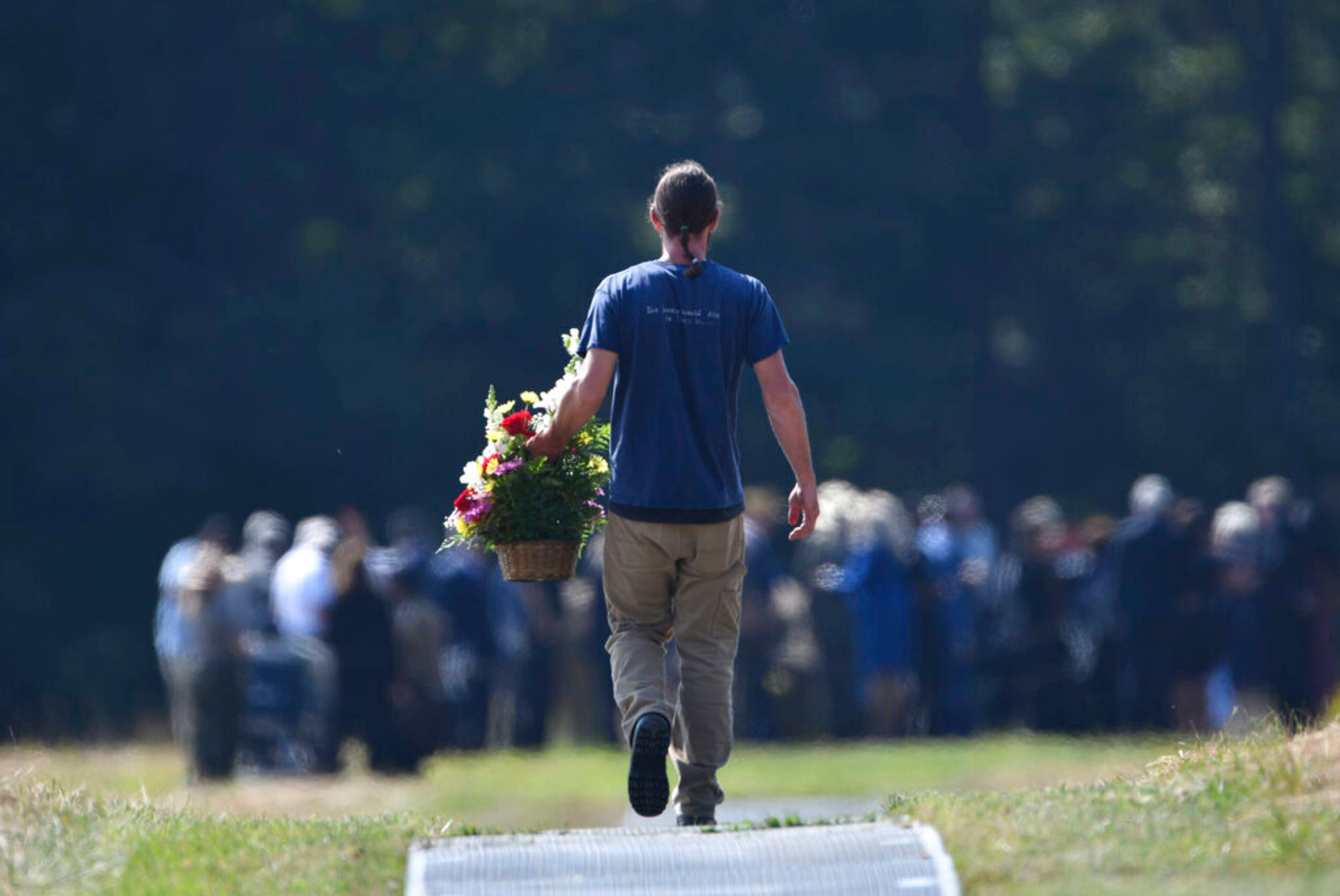 Daniel White of Hamburg, NY., carries a flower arrangement out to the crash site at the 18th annual remembrance ceremony at the Flight 93 National Memorial in Shanksville, Pa., Wednesday, Sept.11, 2019. White's second cousin Louis Joseph Nacke II was killed in the crash. (John Rucosky/Tribune-Democrat via AP)
