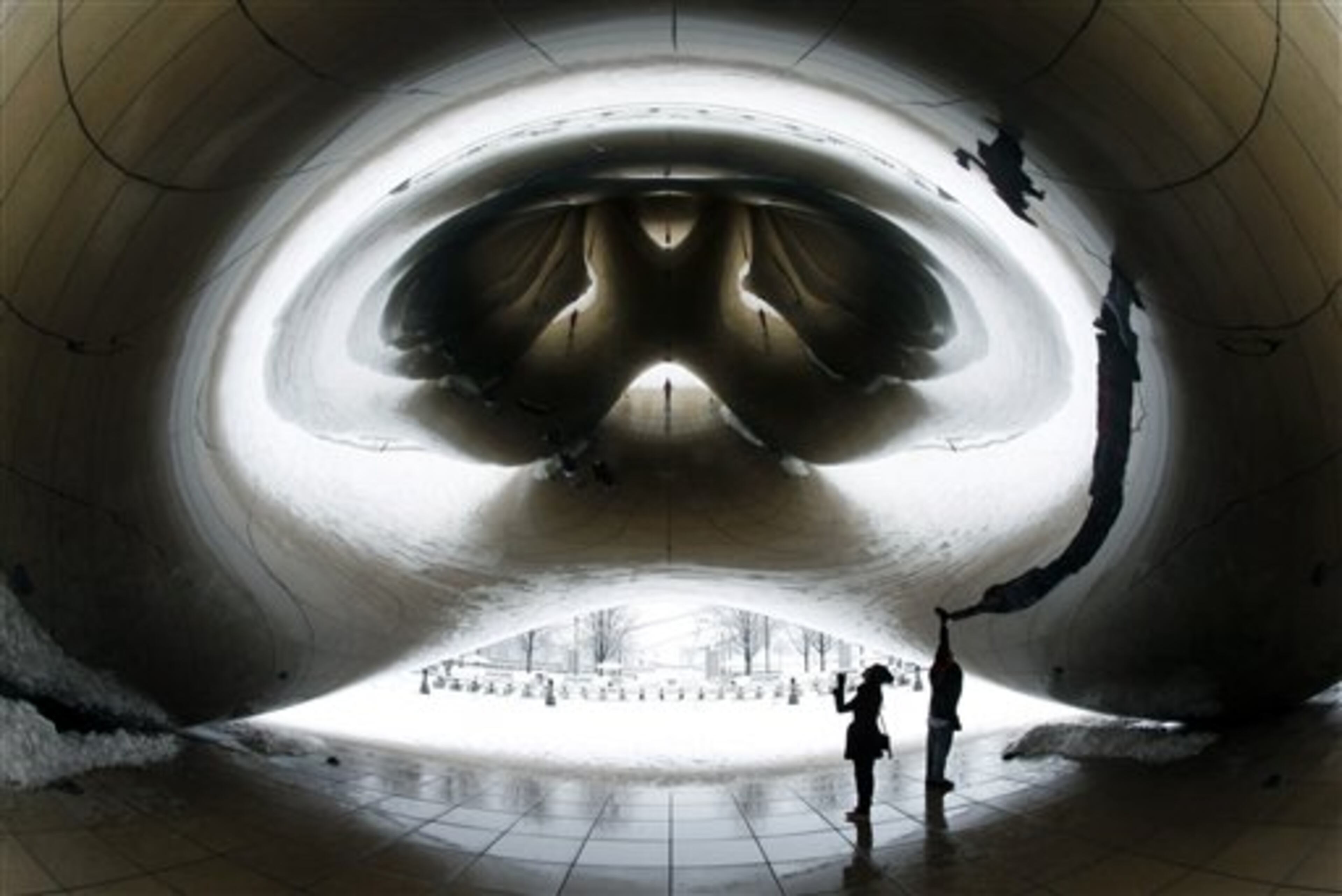 Stacy Crain and Al Giannini, both from Rockford, Ill., walk under Anish Kapoor's stainless steel Cloud Gate sculpture in Chicago's Millennium Park, as a winter storm of rain and snow begins Tuesday, Feb. 26, 2013. Forecasters expect the storm to leave behind three to six inches of snow in the greater Chicago area. (AP Photo/Charles Rex Arbogast)