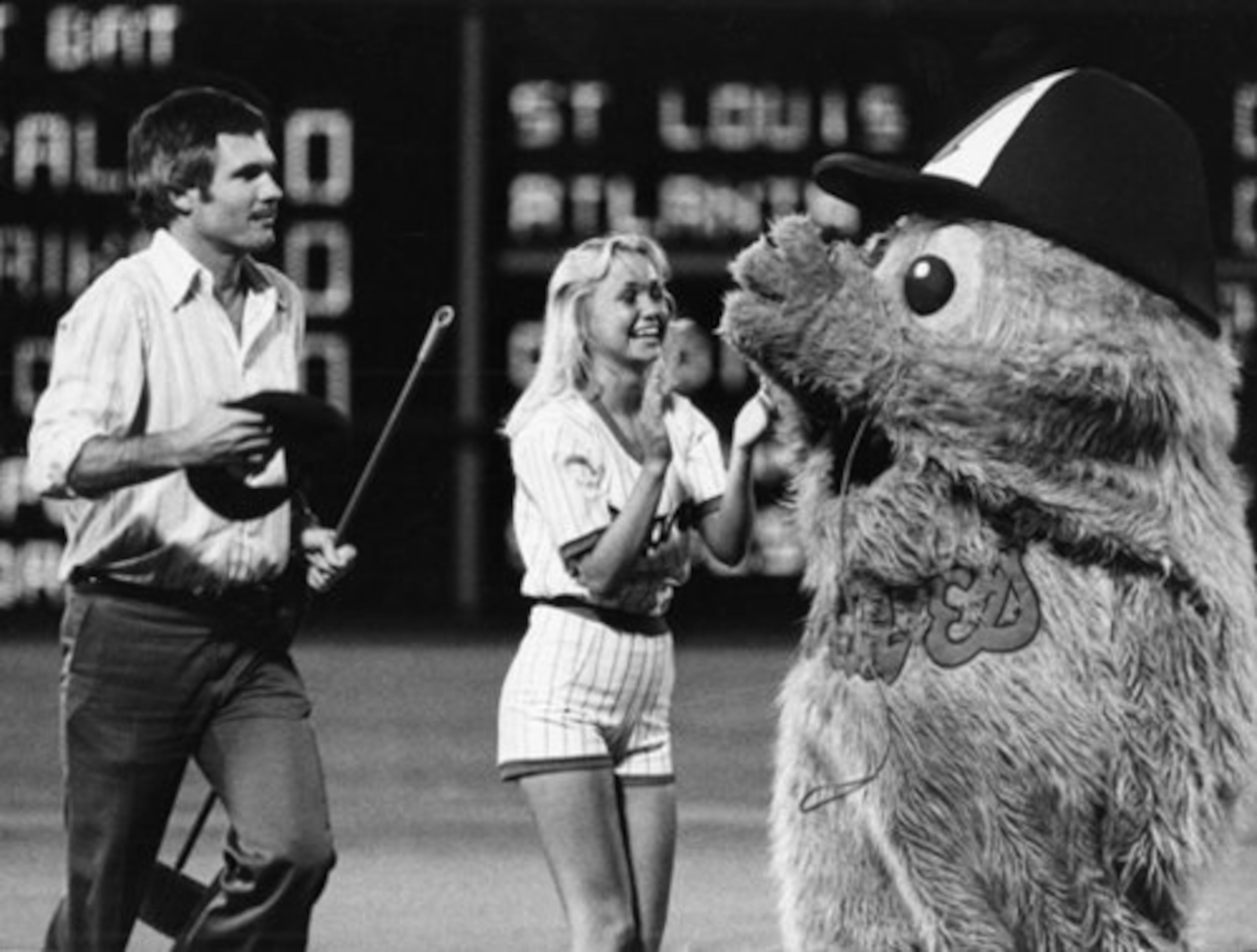 Ted Turner helps out a base sweeper during a Braves game. (AJC File)