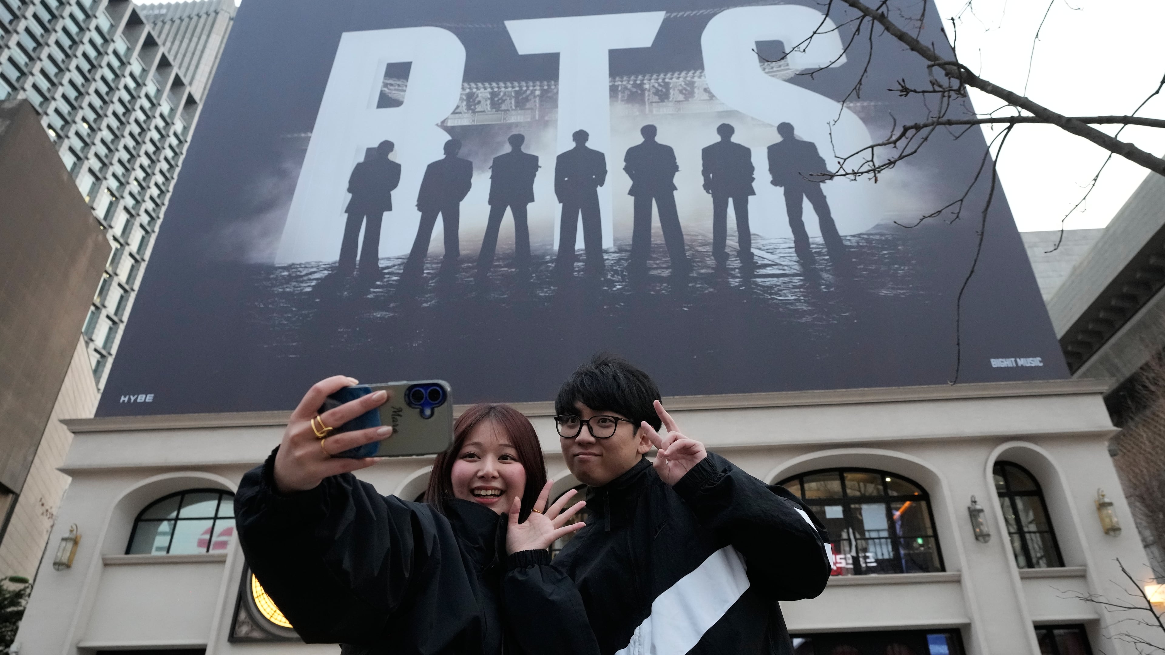 A couple takes a selfie photo near a banner promoting a comeback concert of K-pop group BTS at Gwanghwamun Square in Seoul, Wednesday, March 18, 2026. (AP Photo/Ahn Young-joon)