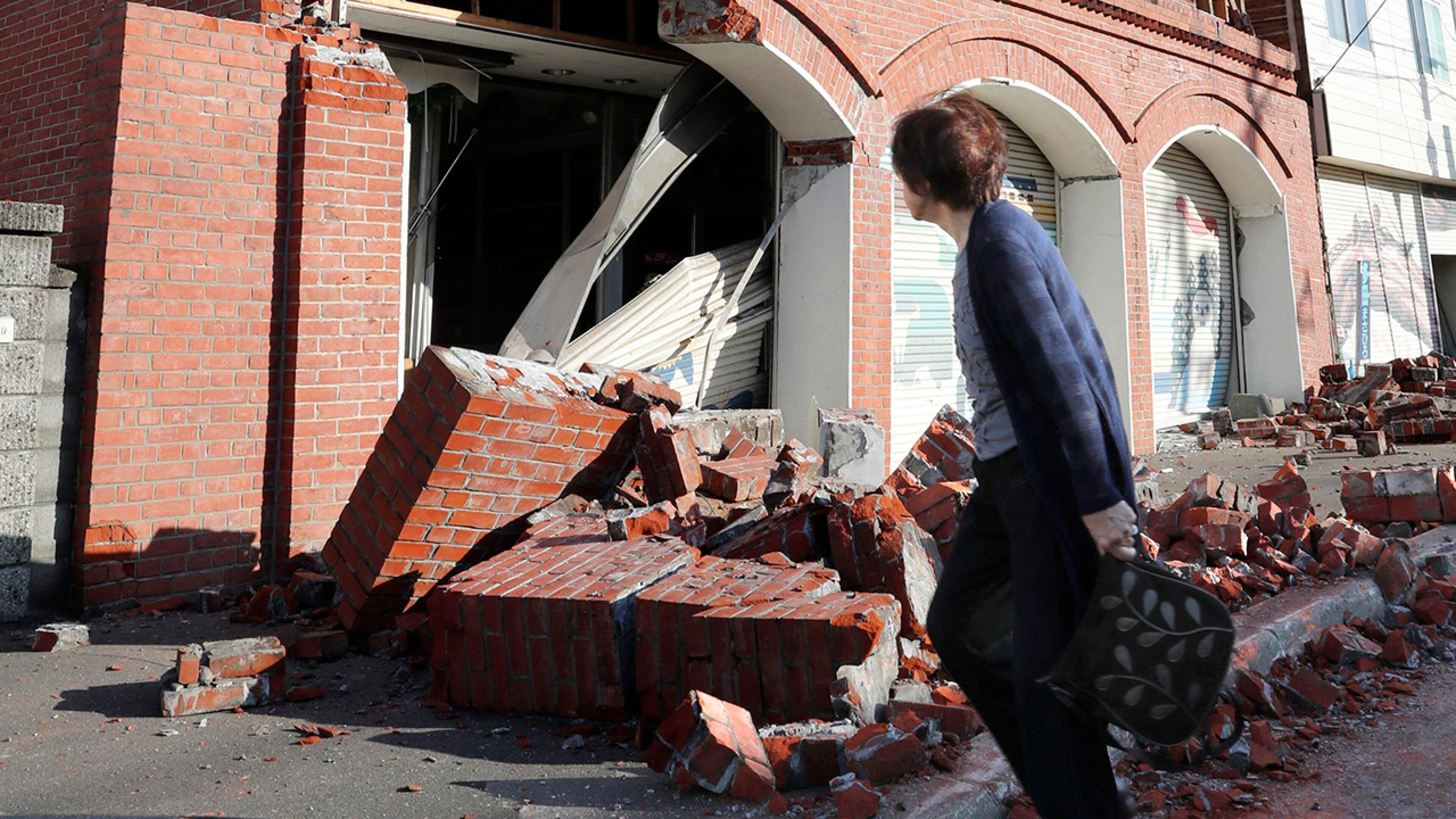 A woman walks past a damaged building in Abira town, near Chitose, Hokkaido, northern Japan following a strong earthquake Thursday, Sept. 6, 2018. A powerful earthquake hit wide areas on Japan's northernmost main island of Hokkaido early Thursday, triggering landslides as well as causing the loss of power at nearly all of 3 million households and a nuclear power plant to go on a backup generator. (Masanori Takei/Kyodo News via AP)