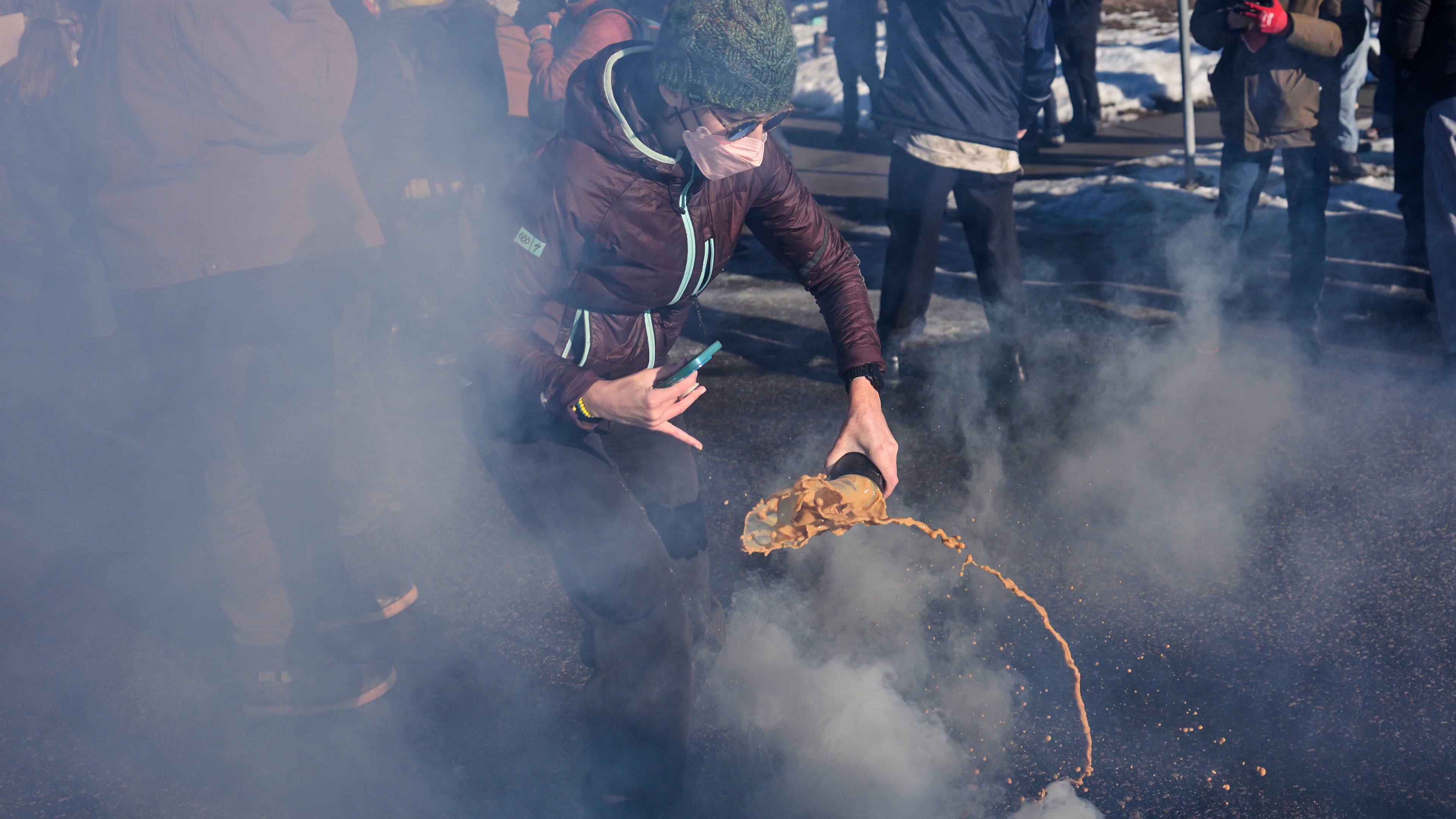 A protester grabs a tear gas grenade deployed by federal immigration officers near the scene where Renee Good was fatally shot by an ICE officer last week, Tuesday, Jan. 13, 2026, in Minneapolis. (AP Photo/John Locher)