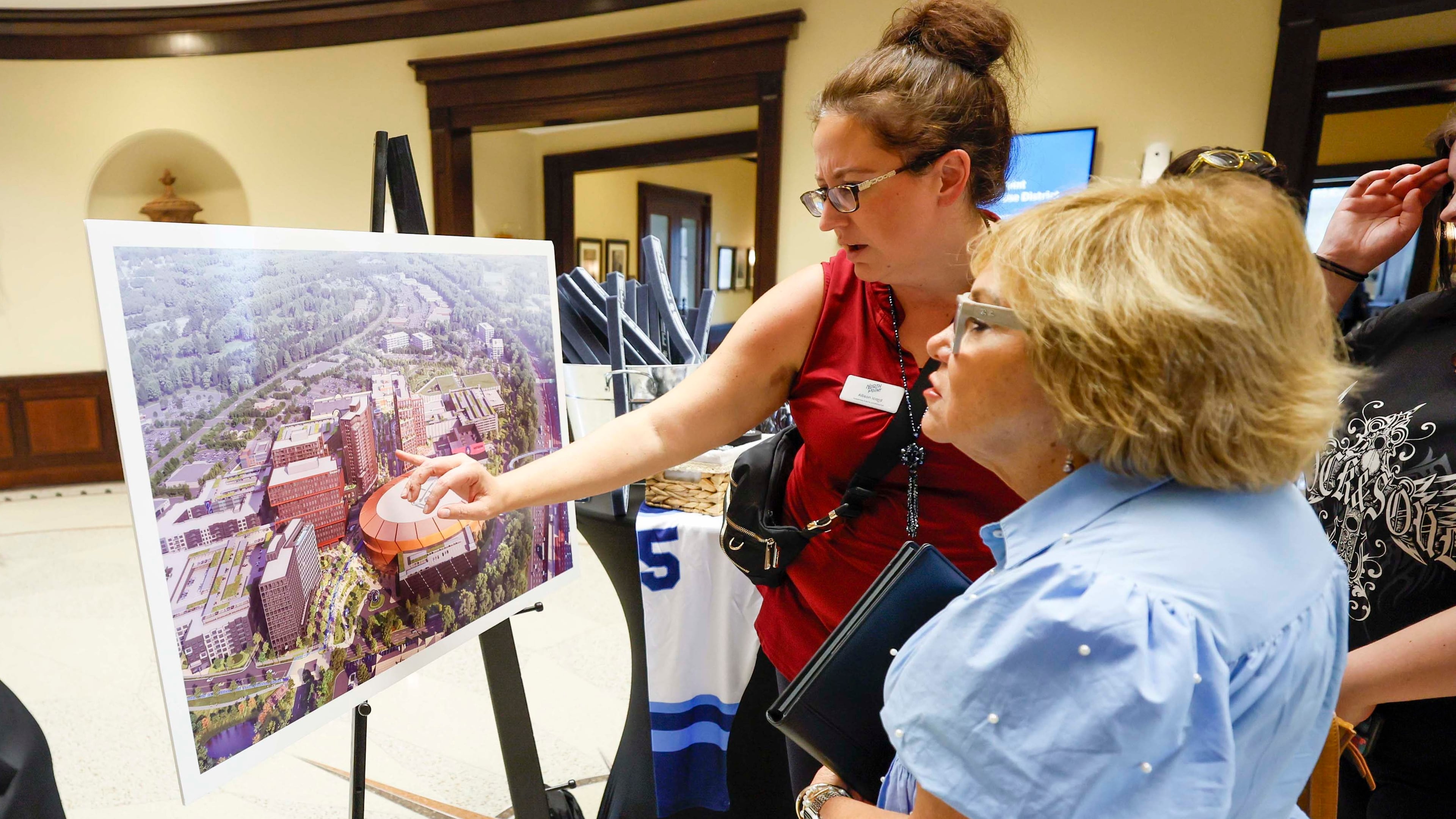 North Point rep Allison Icard presents a rendering of the redevelopment design for North Point Mall to Robbie Rebekah Gring in the Alpharetta City Hall Council Chamber on Monday, Aug. 24, 2026, before a public hearing where the city voted to clear the way for the mall's redevelopment into a sports-anchored entertainment district if the NHL awards the effort an expansion team. (Miguel Martinez/AJC)