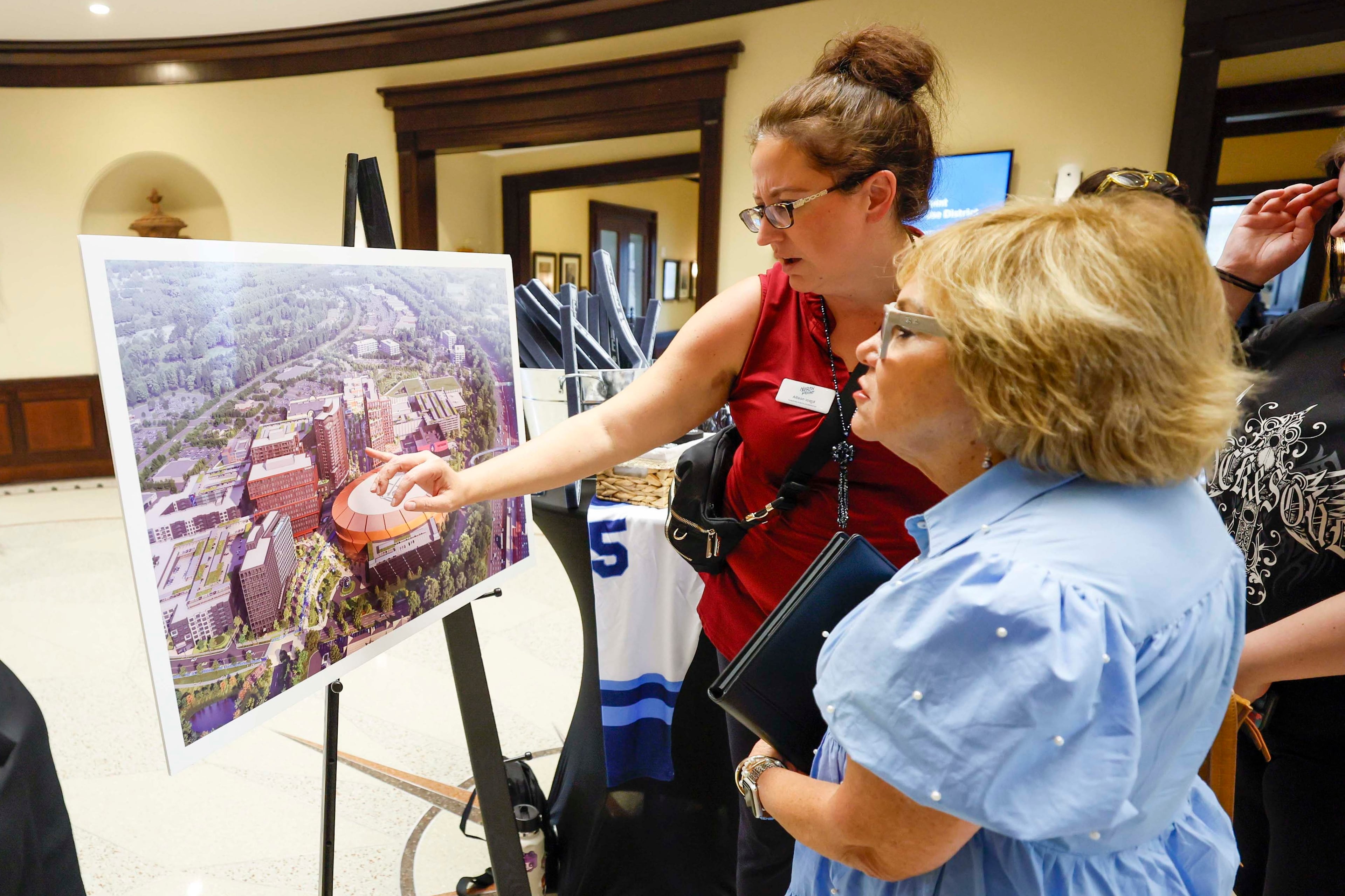 North Point rep Allison Icard presents a rendering of the redevelopment design for North Point Mall to Robbie Rebekah Gring in the Alpharetta City Hall Council Chamber on Monday, Aug. 24, 2026, before a public hearing where the city voted to clear the way for the mall's redevelopment into a sports-anchored entertainment district if the NHL awards the effort an expansion team. (Miguel Martinez/AJC)