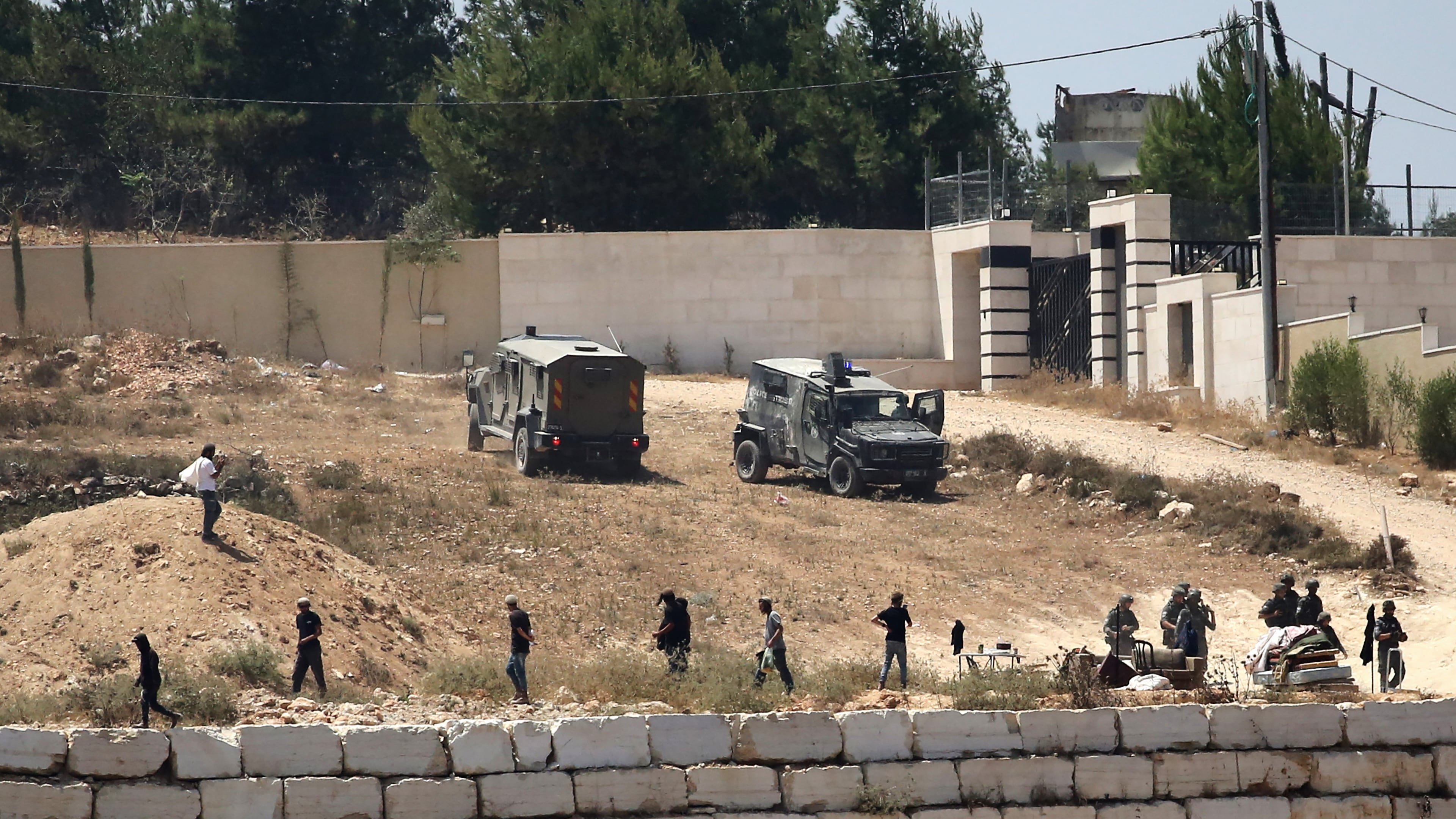 Israeli soldiers stand guard next to settlers in front of Palestinian homes that they have blockaded in the village of Qusra, south of Nablus, in the occupied West Bank, Wednesday, Aug. 12, 2026. (AP Photo/Nidal Eshtayeh)