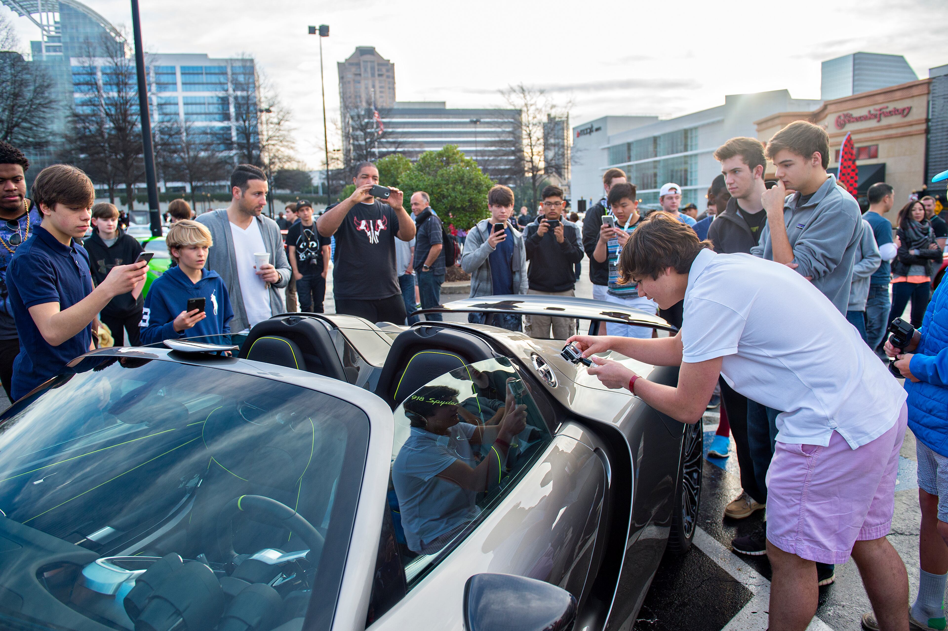 Mason Mamoun (right) leans over a Porshe 918 Spyder to take a photo during the Caffeine & Exotics Car Show at Lenox Square Mall in Atlanta. JONATHAN PHILLIPS / SPECIAL