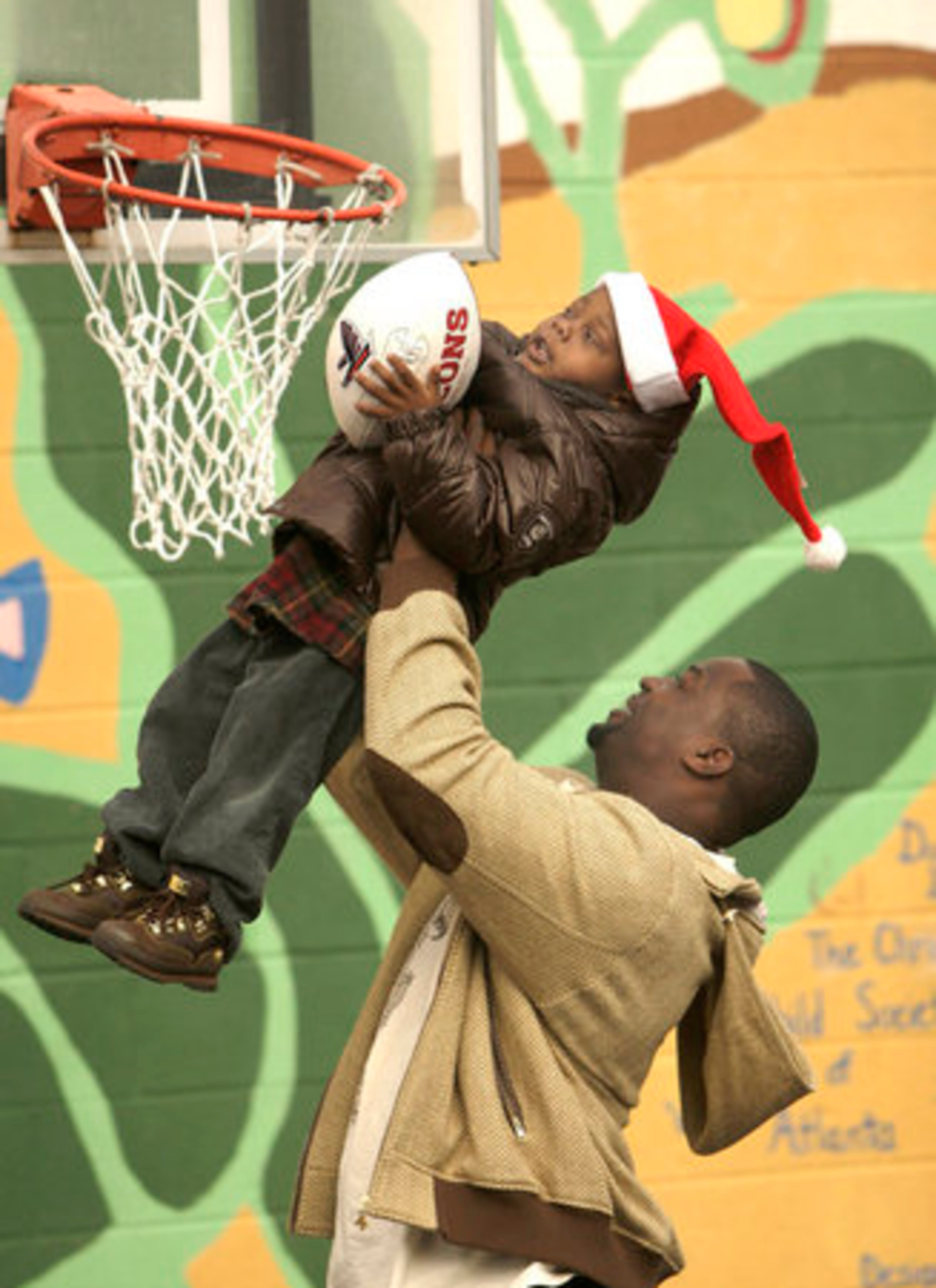 Atlanta Falcon Chauncey Davis picks up 3-year-old Robert Lyons to help him dunk a football at the Atlanta Day Shelter for Women and Children on Tuesday. Davis and teammates Jonathan Babineaux and Kindal Moorehead played and signed autographs for the children and their mothers during their visit at the Midtown shelter.