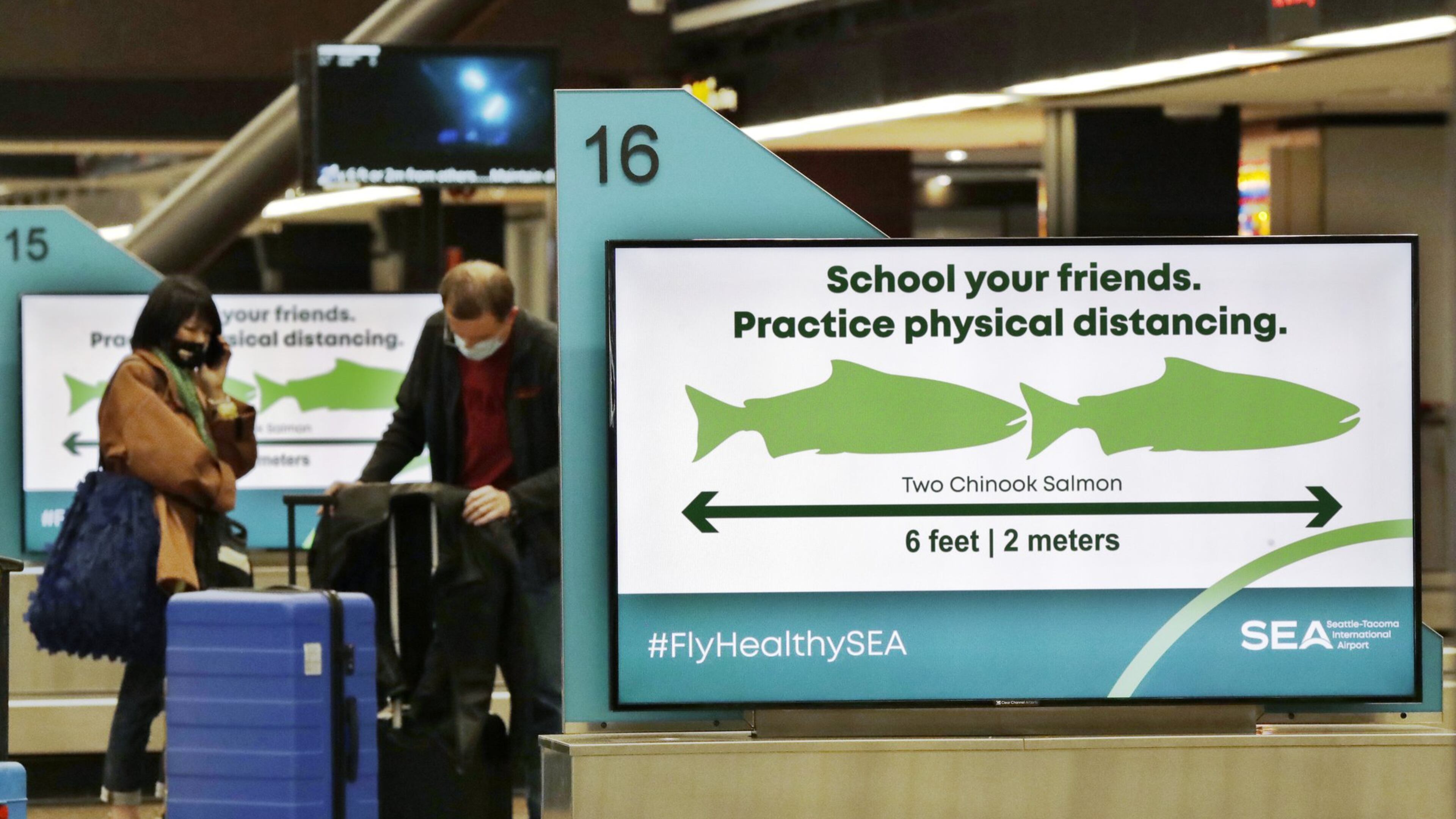 Travelers pick up luggage where signs remind them to stay six feet apart at Seattle-Tacoma International Airport Monday, May 18, 2020. (AP Photo/Elaine Thompson)