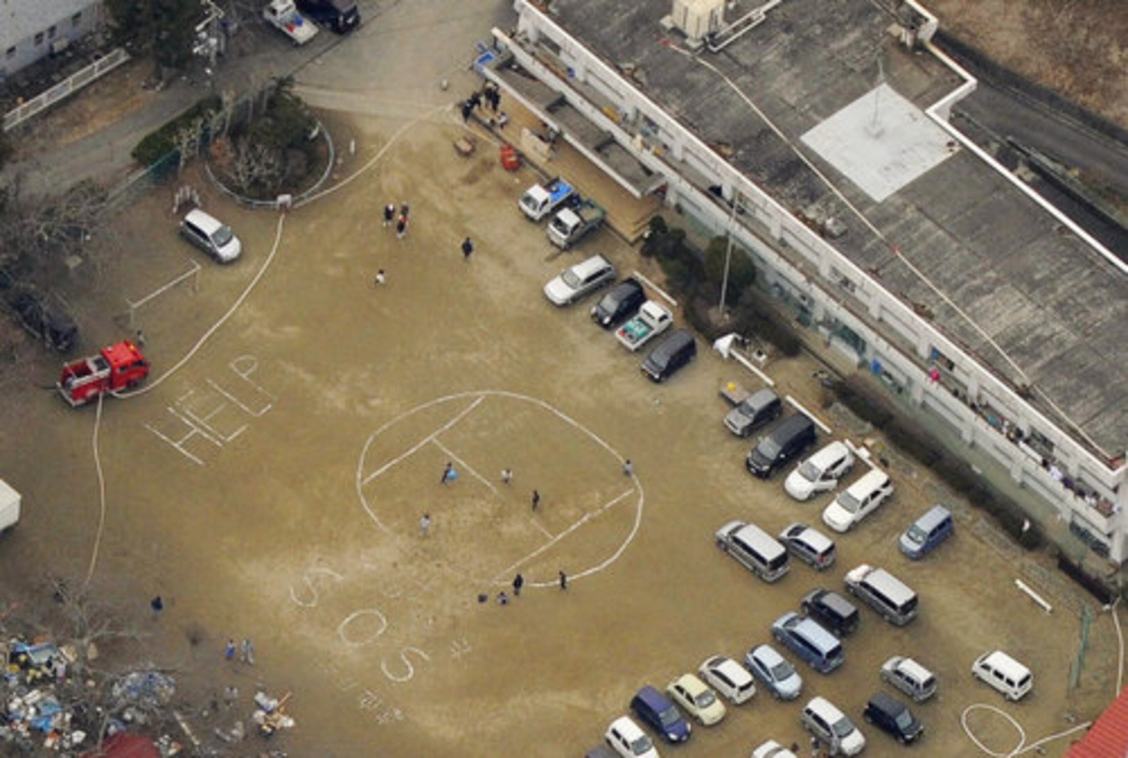 Signs of "HELP" and "SOS" are written on the ground of Ohara Primary School in Ishinomaki, Miyagi Prefecture, on Monday.