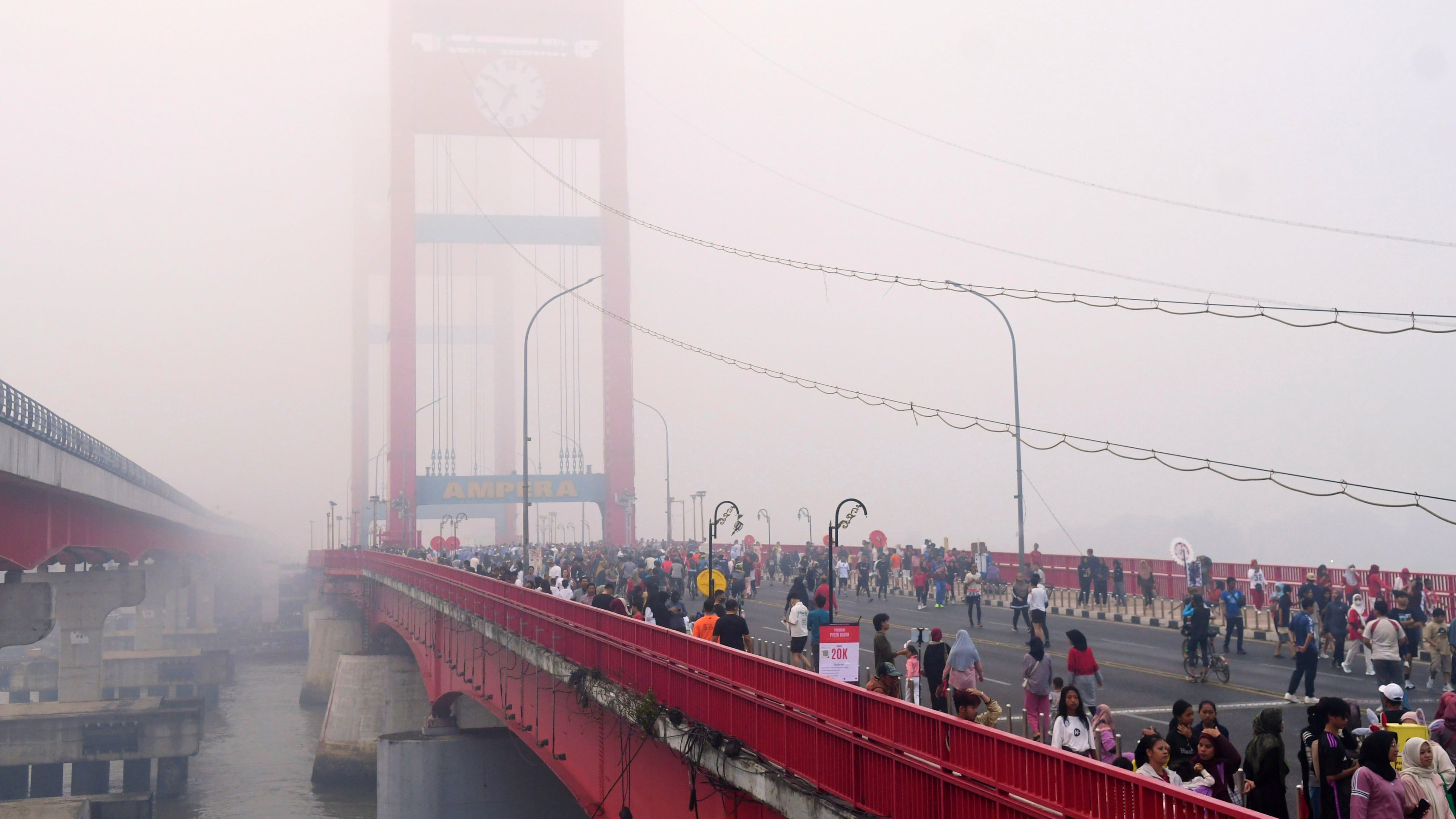 People walk along the Ampera Bridge as haze from wildfires blankets the city of Palembang, in South Sumatra, Indonesia, Sunday, Aug. 23, 2026. (AP Photo/Muhammad Fajri)