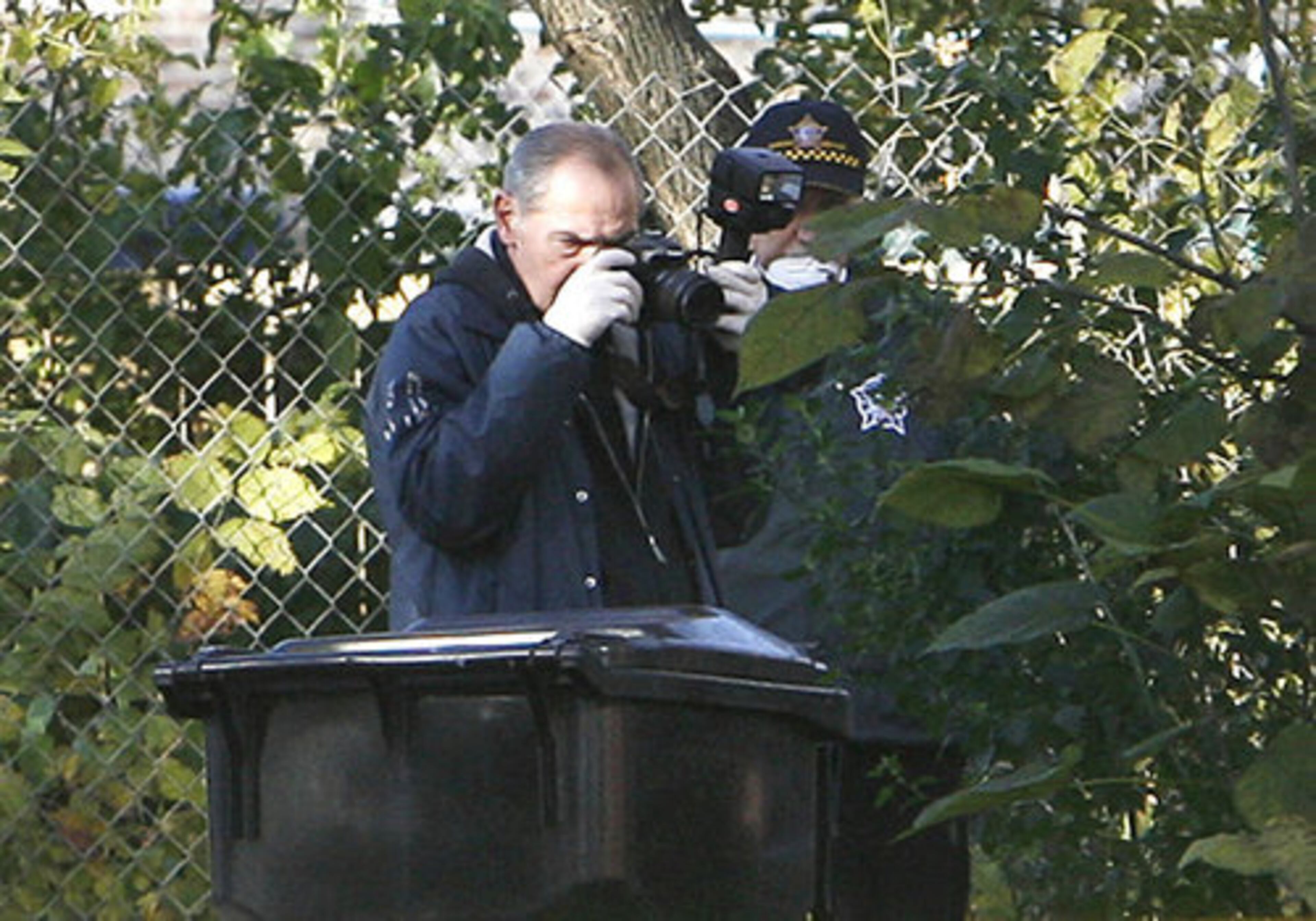 A Chicago Police Department photographer takes pictures near a trash can on the city's West Side, Wednesday, Oct. 29, 2008, where they were searching for evidence near the site where 7-year-old Julian King was found shot to death in an SUV on Monday.