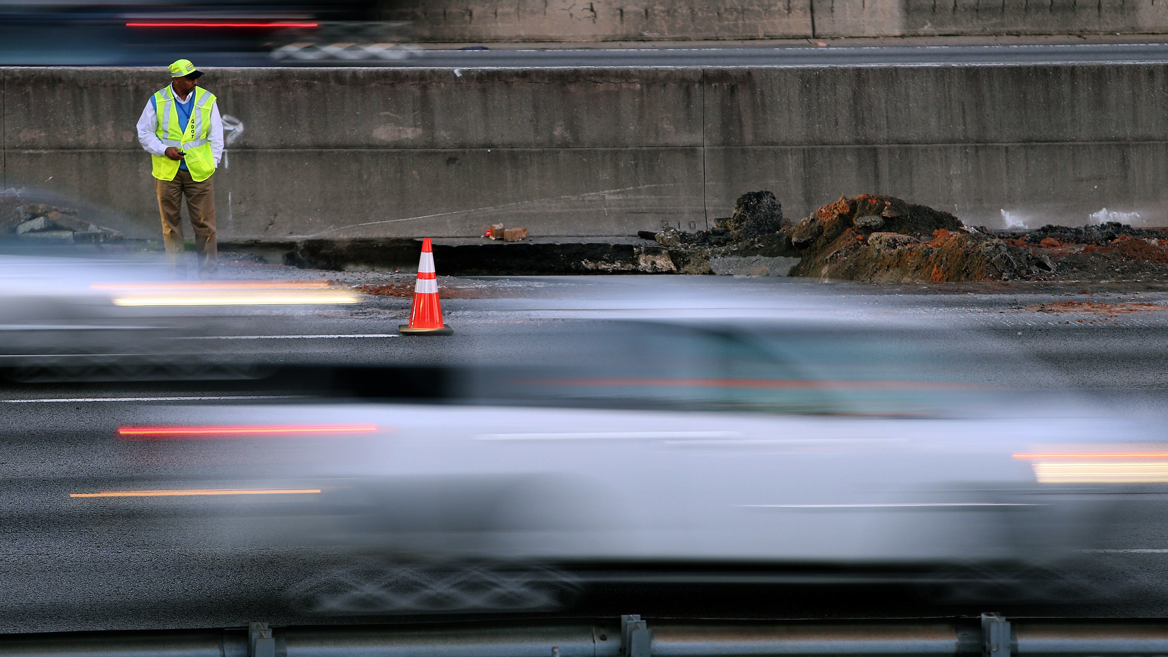 Traffic streams past a Georgia DOT worker at the scene of a drain structure collapse on I-85 South just North of Clairmont Road on Monday evening October 7, 2013. Crews were planning to work through the night to repair the road, but expect that two lanes, including the HOV lane, will be closed through the morning rush hour.