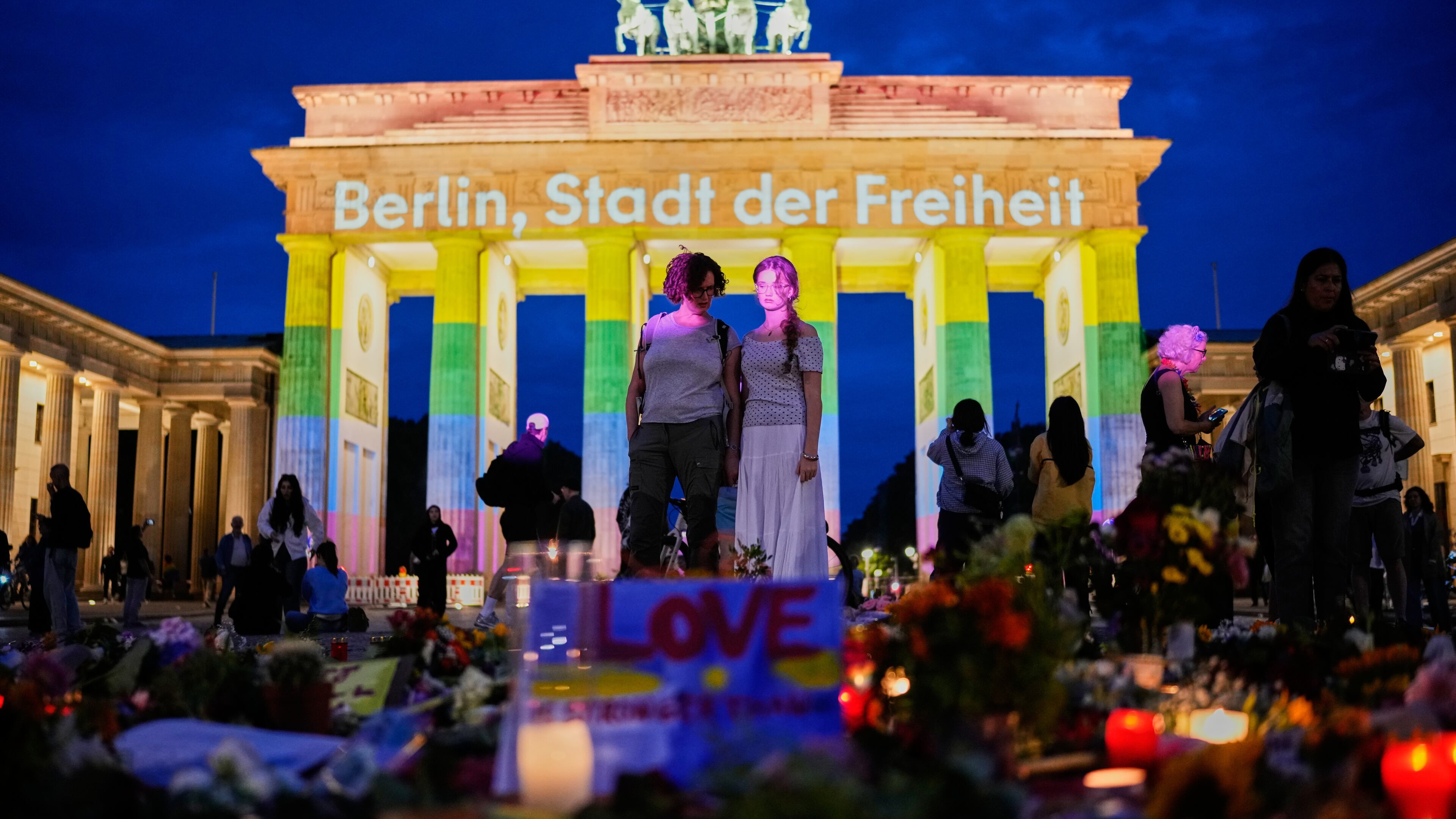 People gather in front of the Brandenburg Gate illuminated with the message "Berlin, city of freedom", commemorating the victims, after a car rammed into a crowd at the Pride March in Berlin, Sunday, July 26, 2026. (AP Photo/Ebrahim Noroozi)