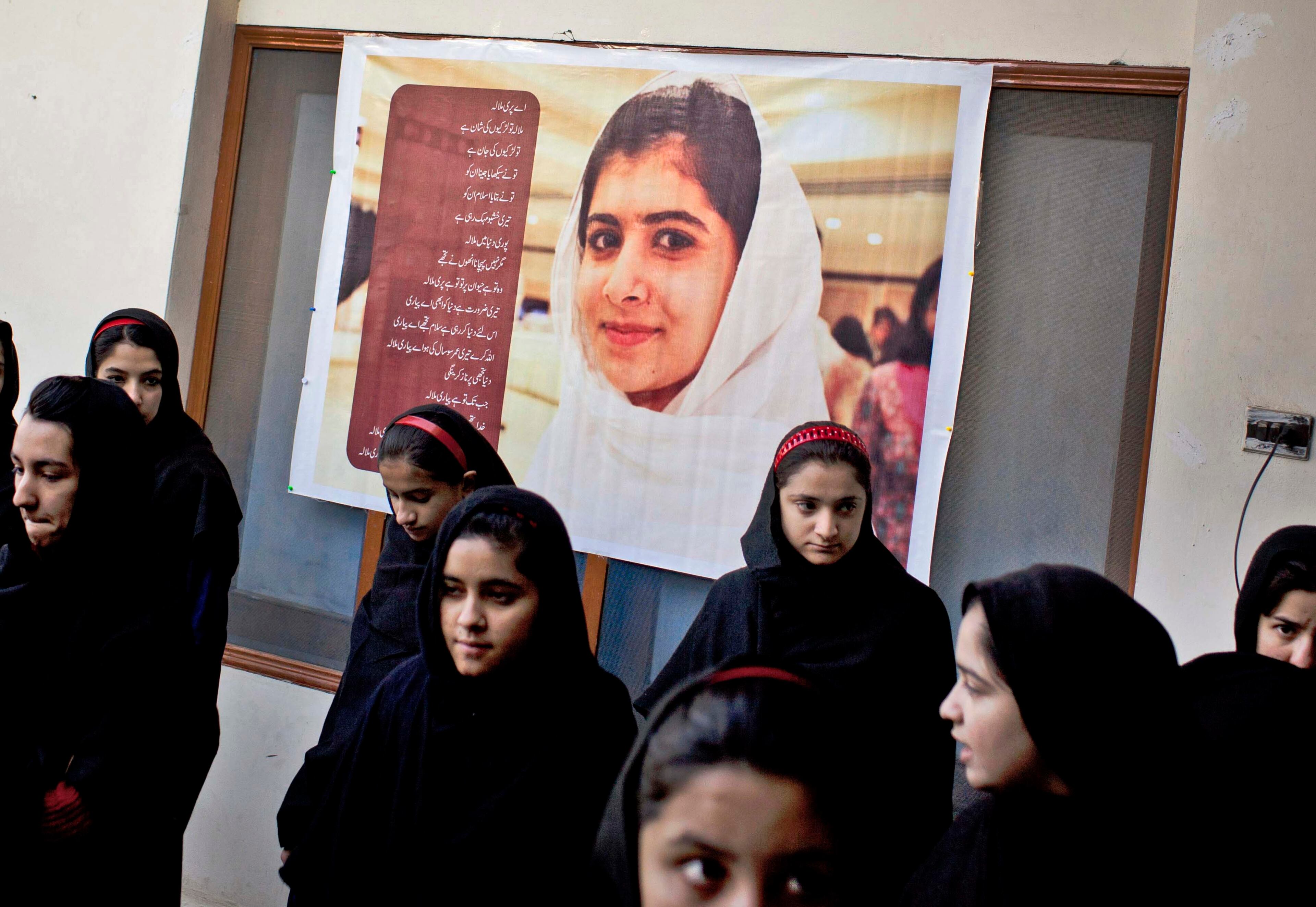 In this Thursday, Nov. 15, 2012 photo, Pakistani girls gather under a poster of Malala Yousufzai in her old school in Mingora, Swat Valley, Pakistan. The giant poster of her that once emblazoned the wall of the assembly hall has been removed. The school made no plans to recognize the anniversary of Malala's shooting by Taliban, teachers and students are afraid.
