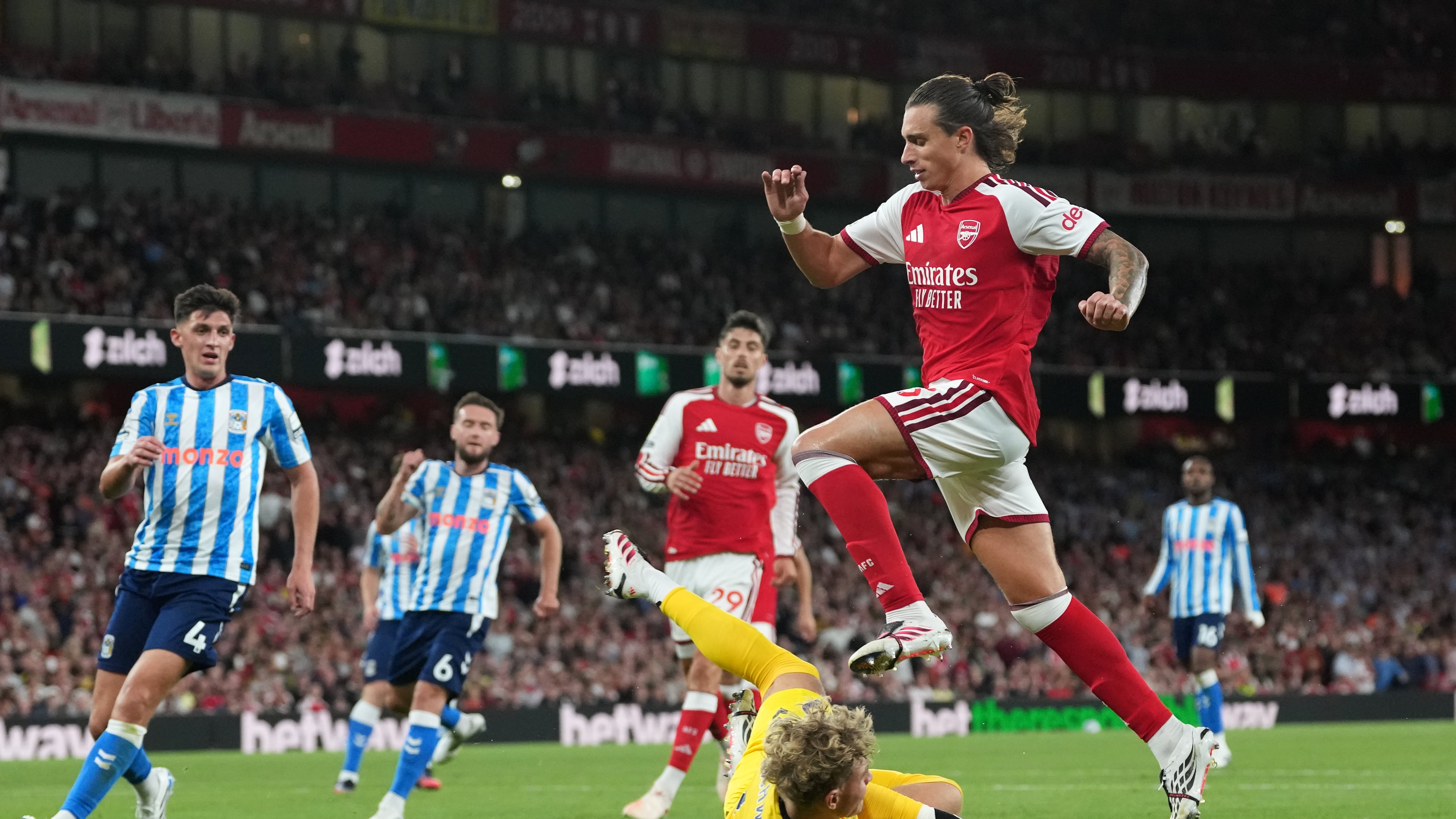 Arsenal's Riccardo Calafiori leaps over Coventry City's goalkeeper Carl Rushworth during the English Premier League soccer match between Arsenal and Coventry City in London, Friday, Aug. 21, 2026. (AP Photo/Kirsty Wigglesworth)
