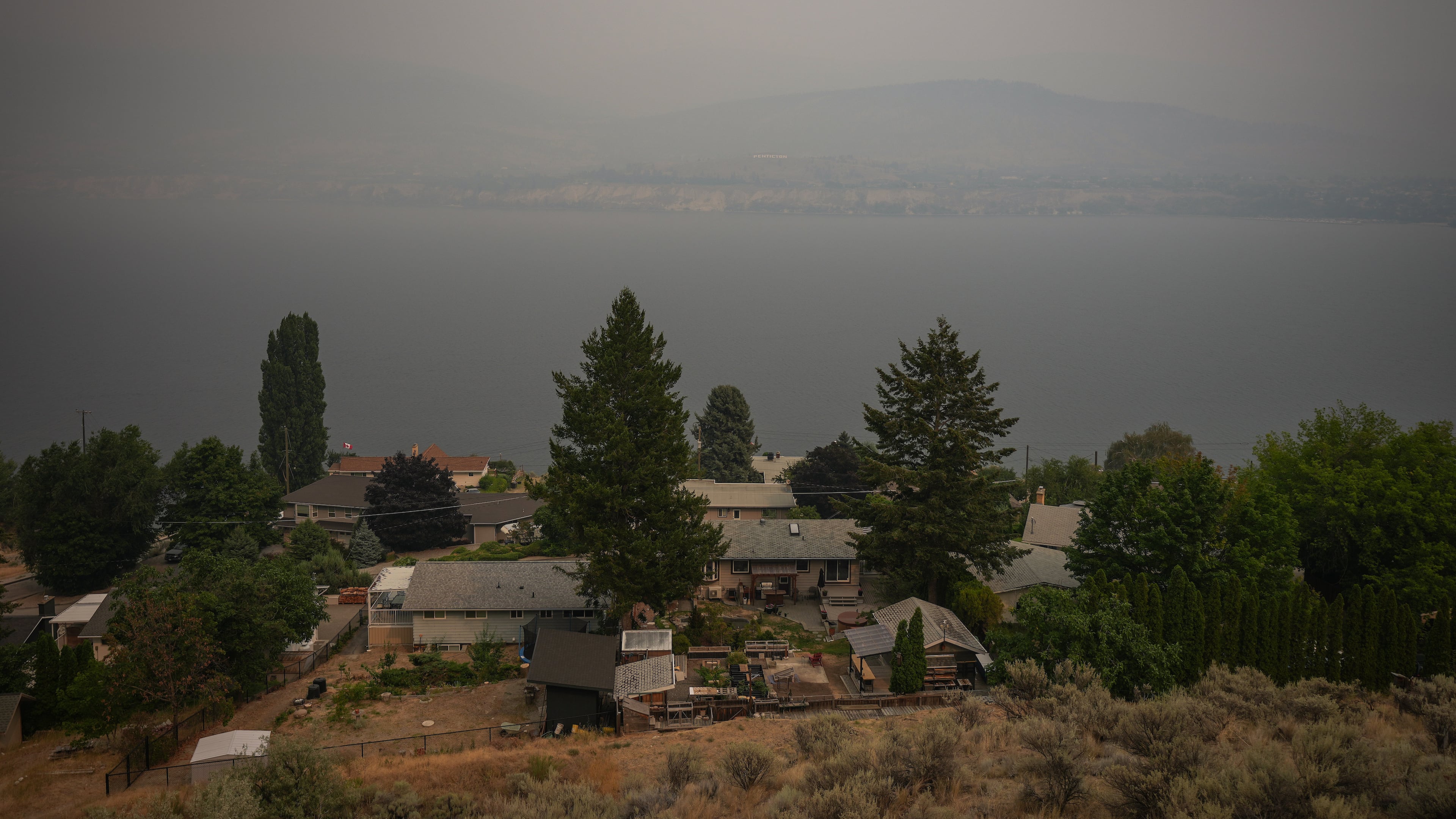 Houses are seen overlooking Okanagan Lake as smoke from the Bald Range wildfire blankets the area, in Penticton, British Columbia, Sunday, Aug. 9, 2026. (Darryl Dyck/The Canadian Press via AP)