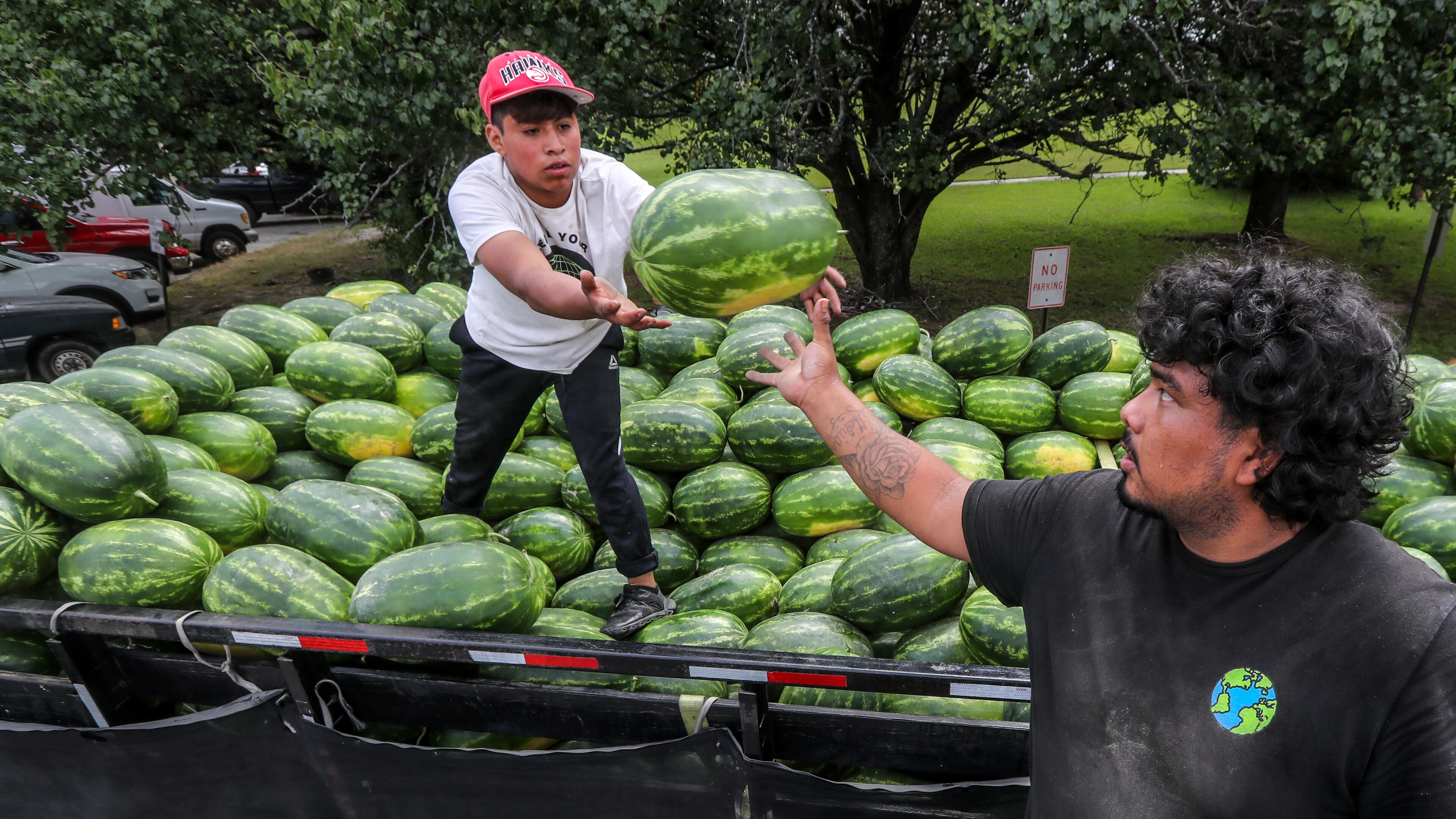 PM Produce workers, Juan Lopez (left) passes off another watermelon to Daniel Valle (right) as they load up another customer at the Atlanta State Farmers Market in Clayton County located at 16 Forest Pkwy in Forest Park.