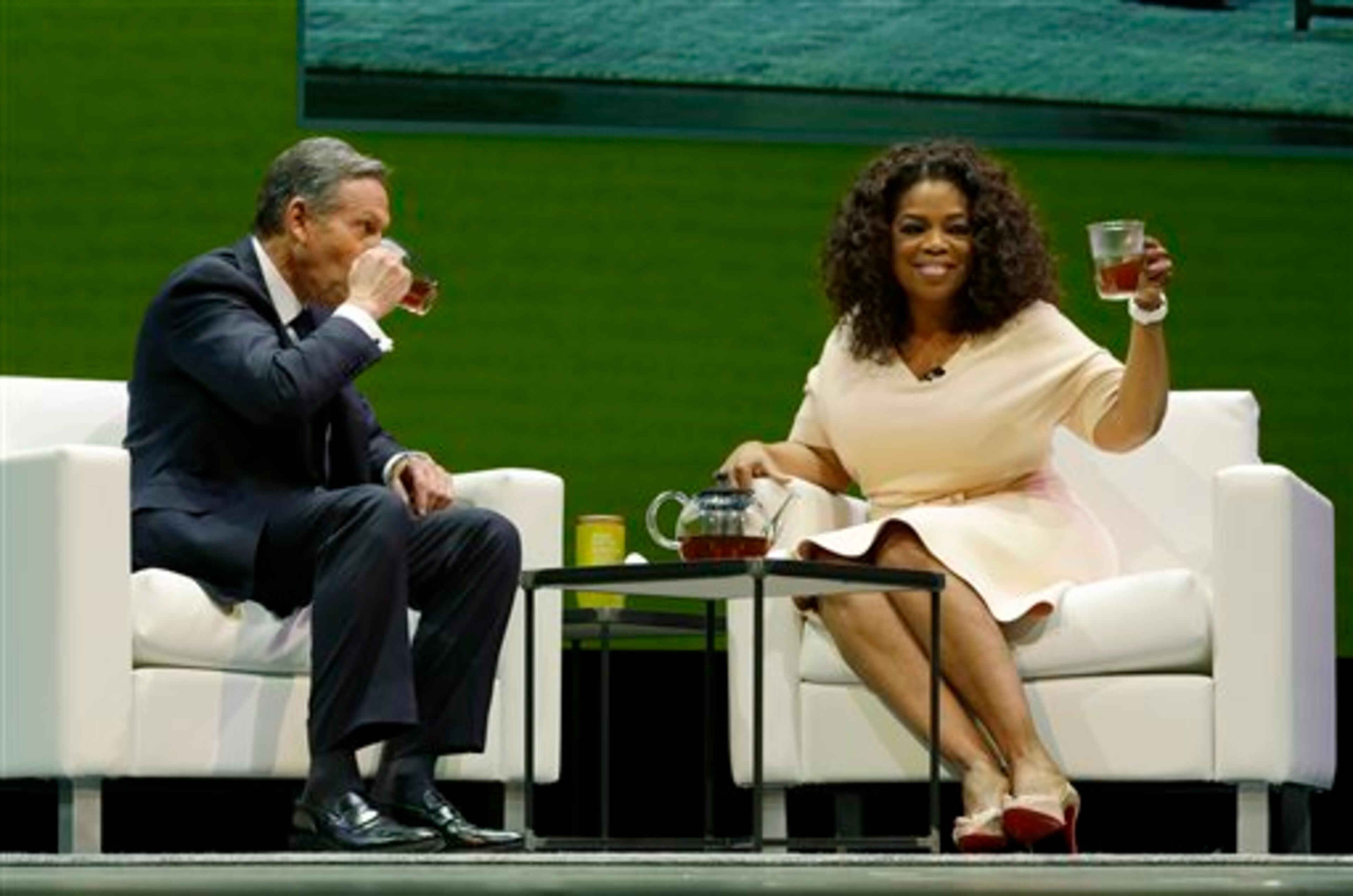 Howard Schultz, left, chairman and CEO of Starbucks Coffee Company, sits and drinks tea with Oprah Winfrey, right, to announce their partnership to offer Teavana Oprah Chai tea, Wednesday, March 19, 2014, at Starbucks' annual shareholders meeting in Seattle. (AP Photo/Ted S. Warren)