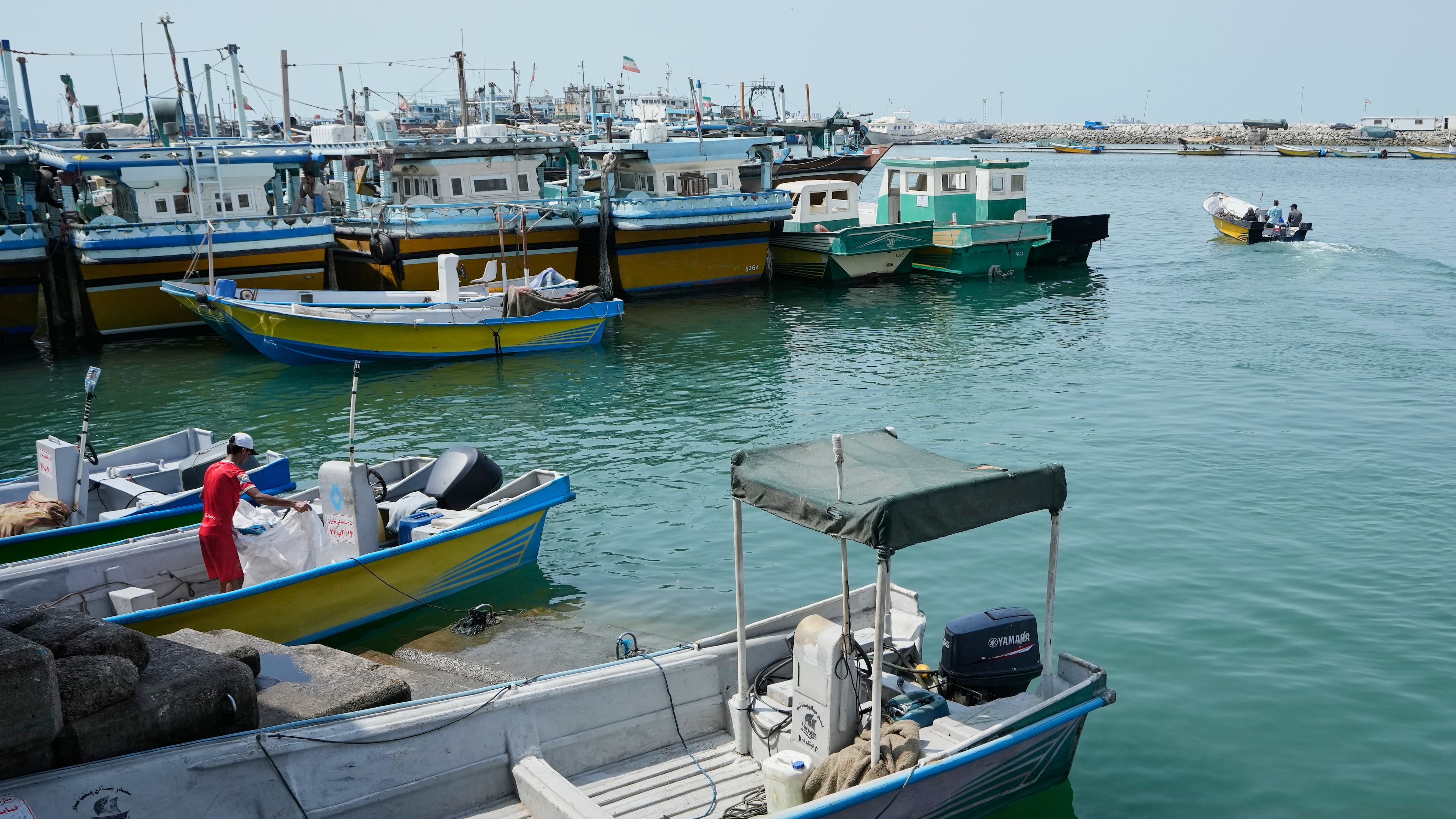 A man works aboard a boat as a motorboat leaves a harbor in Bandar Abbas, Iran, Sunday, Sept. 6, 2026. (AP Photo/Vahid Salemi)
