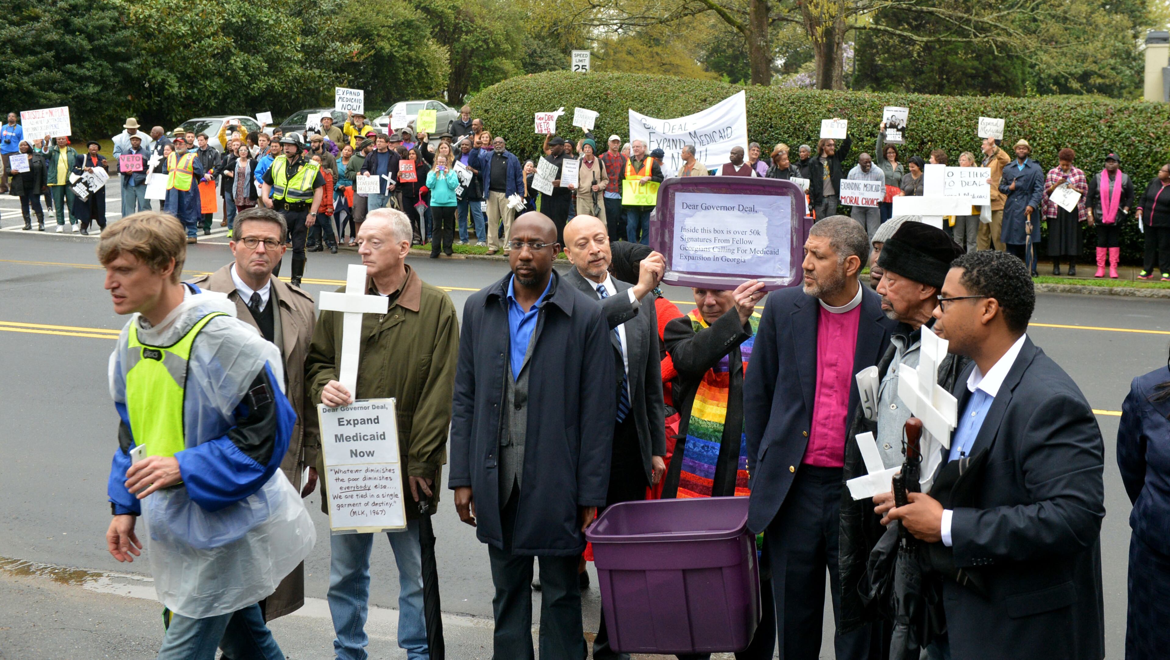 Demonstrators and clergy stand at the gates to the Governor's Mansion. A crowd that swelled to more than 100 protesters included several Atlanta clergy members outside the Governor's Mansion on W. Paces Ferry Road Monday, April 7, 2014. Protesters were calling on Governor Nathan Deal to expand Medicaid services in the state. KENT D. JOHNSON / KDJOHNSON@AJC.COM