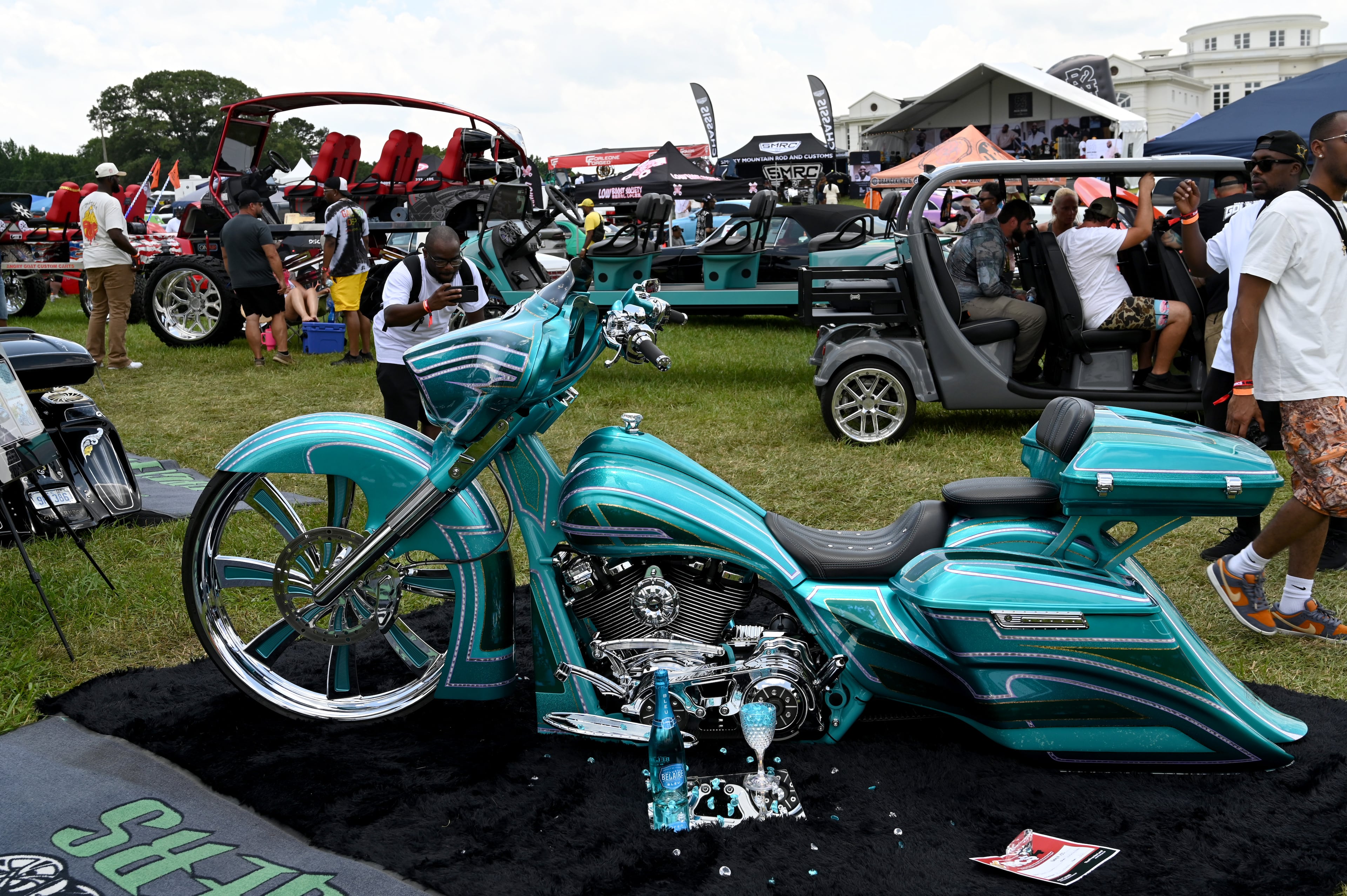 Attendees walk through fleets of classic and custom automobiles, luxury vehicles, boats, RVs and trailers during the 4th Annual Rick Ross Car and Bike Show, Saturday, June 7, 2025, in Fayetteville. The 4th Annual Rick Ross Car and Bike Show will include a vendor market with more than 30 vendors, food trucks, fleets of classic/custom automobiles, luxury vehicles, boats, RVs and trailers on the front of the mansion. Stage performances include Plies, Ross' new signee Nino Breeze and Ross himself. (Hyosub Shin / AJC)
