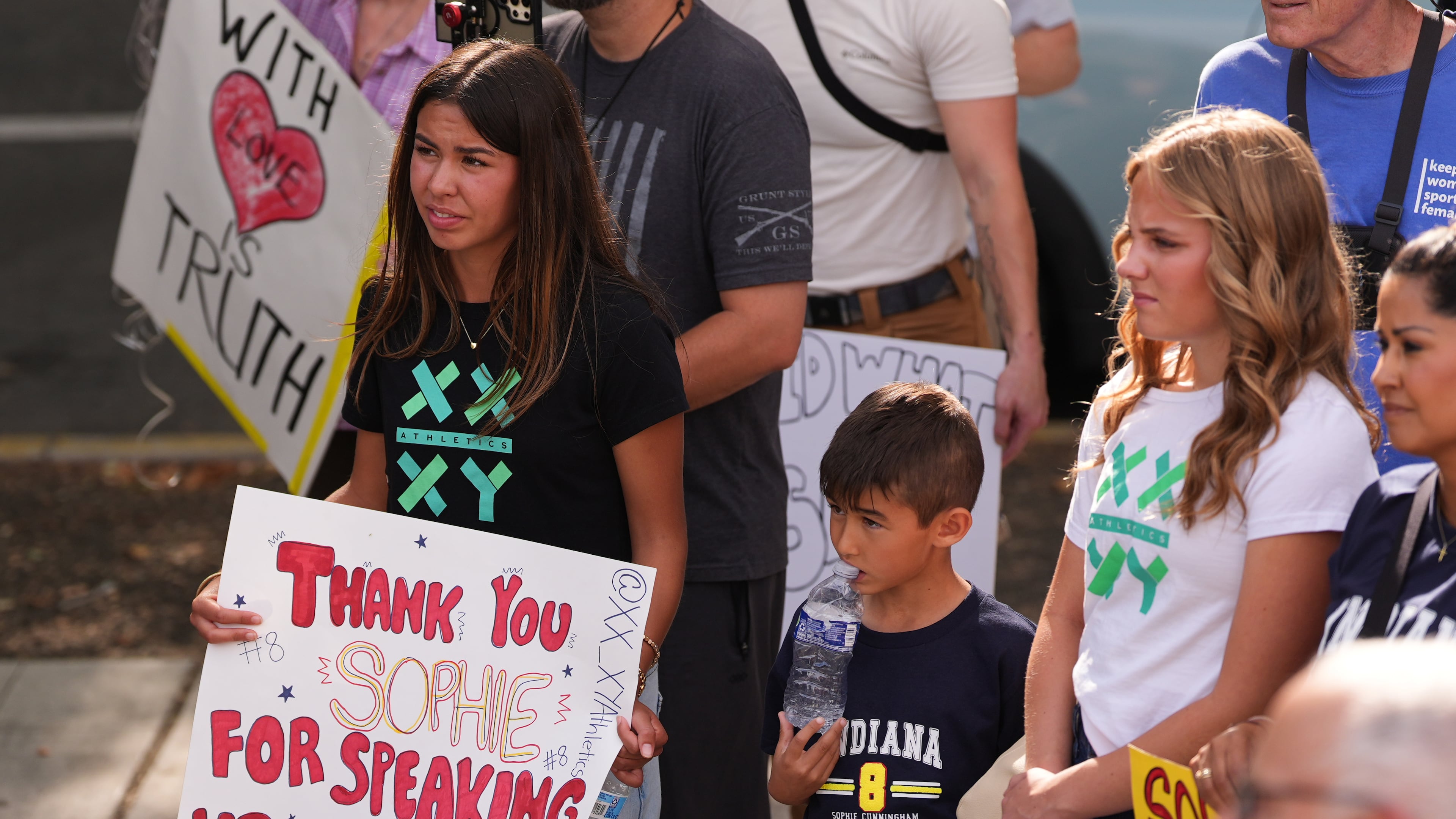 Ahnaleigh Wilson, 17, a track athlete who says she has competed against and placed behind transgender athletes at meets, holds a sign for Indiana Fever guard Sophie Cunningham during a rally before a WNBA basketball game between the Fever and the Seattle Storm, Tuesday, July 28, 2026, in Seattle. (AP Photo/Lindsey Wasson)