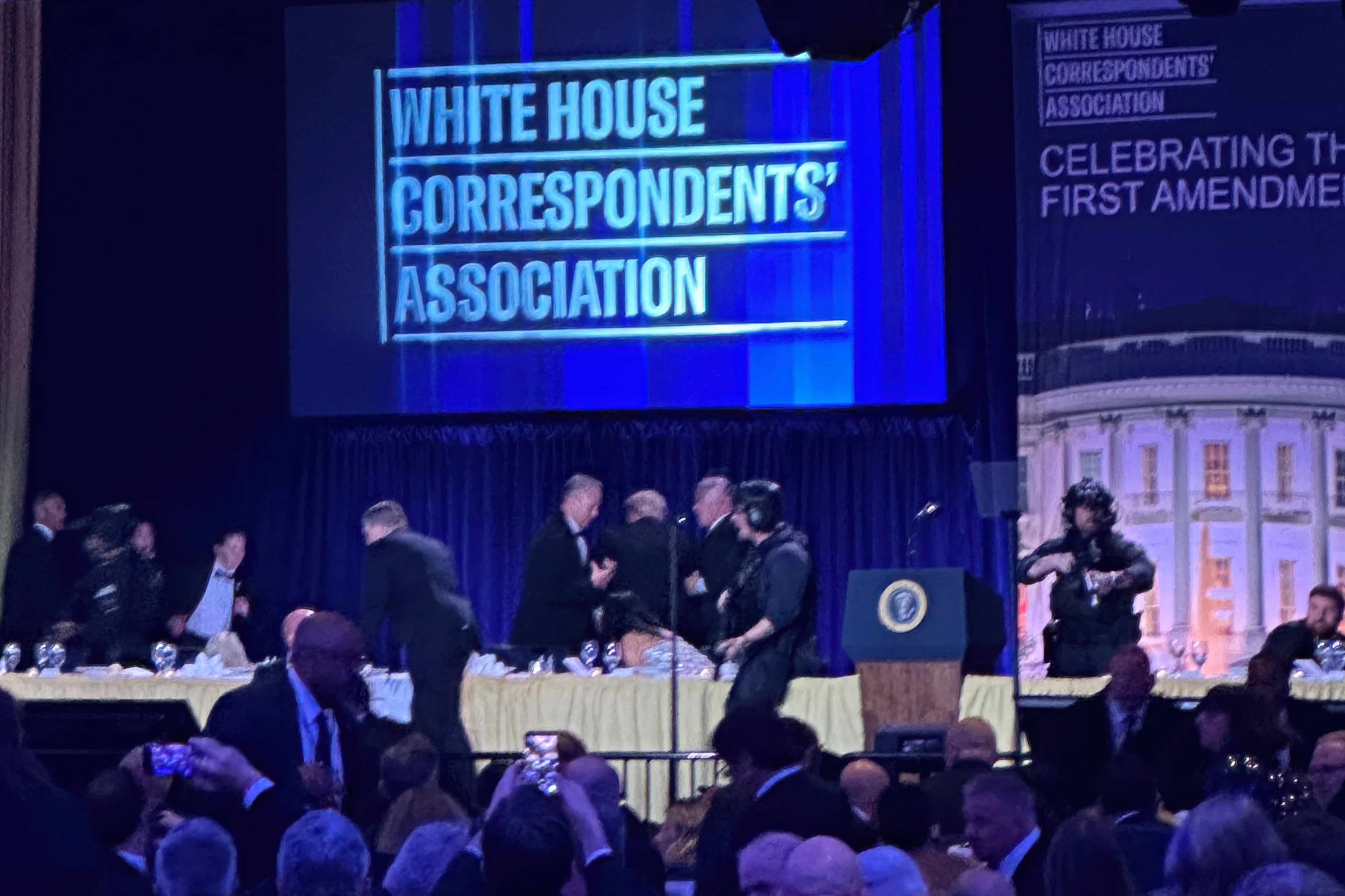 U.S. Secret Service agents surround President Donald Trump as he is taken from the stage after a shooting incident outside the ballroom during the White House Correspondents Dinner, Saturday, April 25, 2026, in Washington. (AP Photo/Alex Brandon)