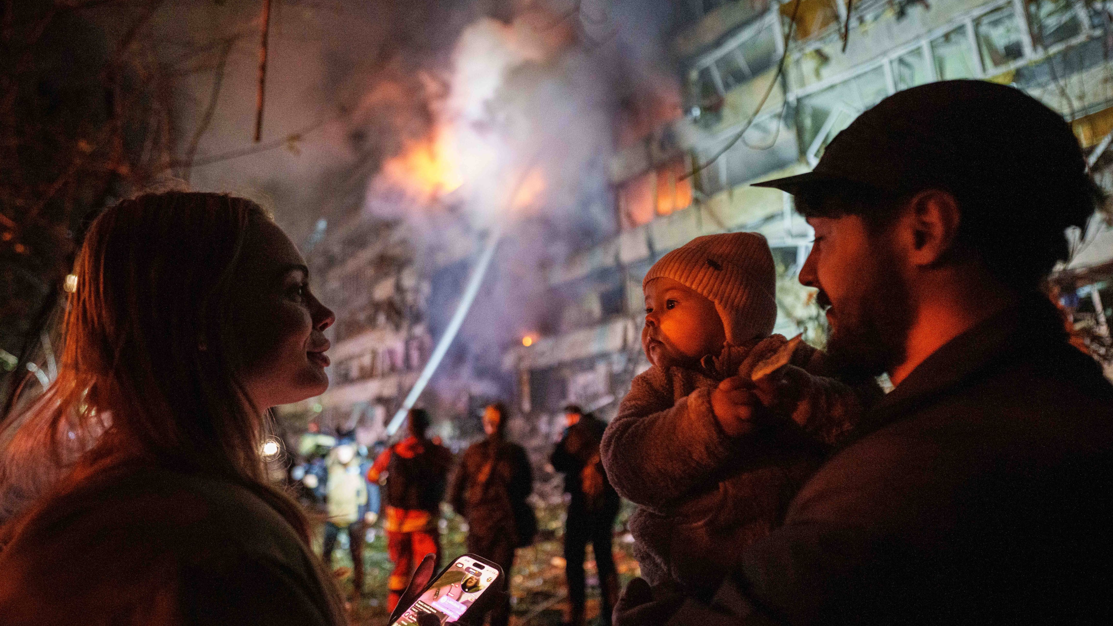Victoria Deineko, her husband Ievhen Deineko and their daughter Mia look at a multi-story residential building damaged in a Russian missile strike in Kyiv, Ukraine, Tuesday, Oct. 13, 2026. (AP Photo/Evgeniy Maloletka)