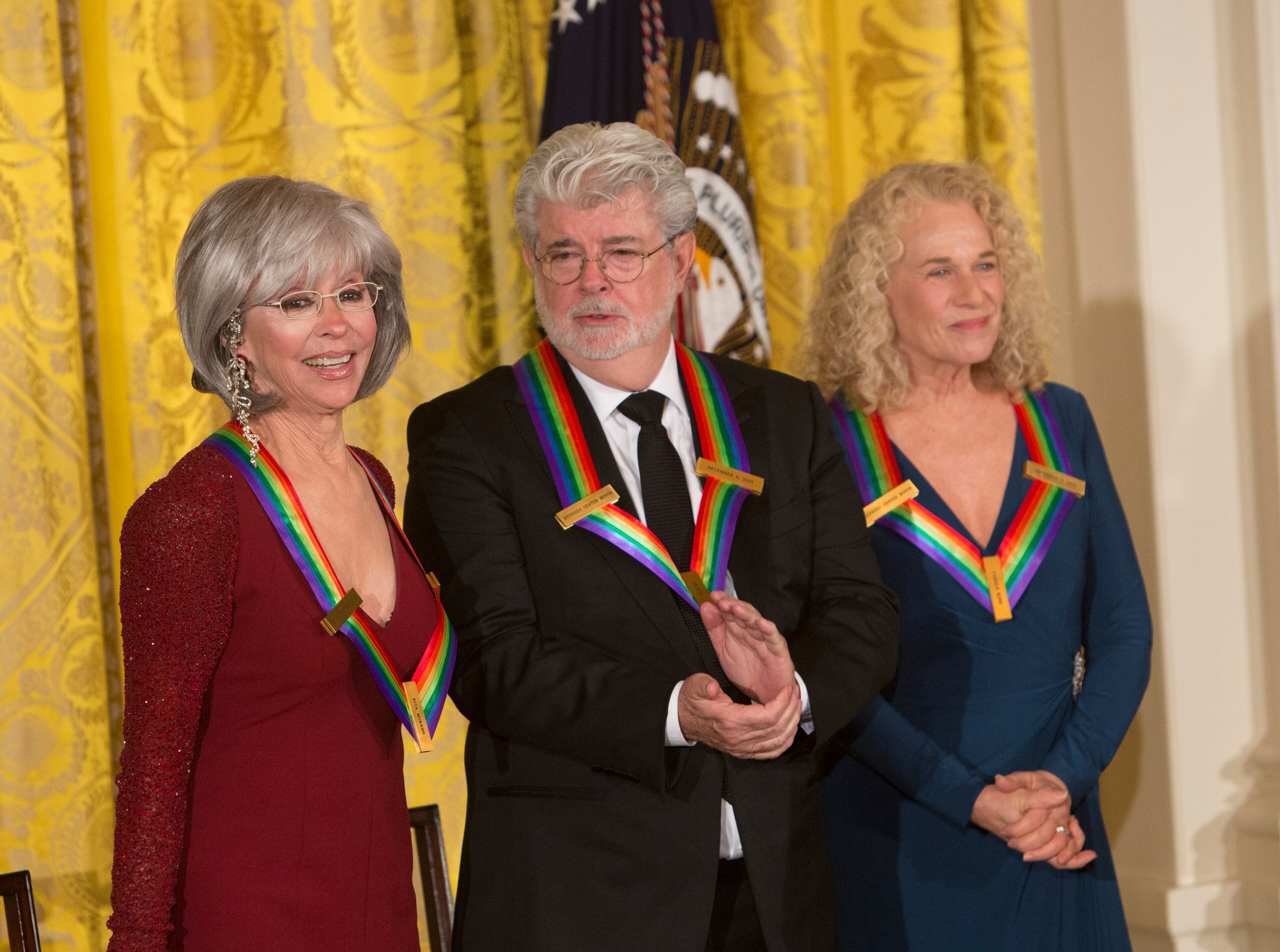 Actress and singer Rita Moreno (Lt), filmmaker George Lucas (C) and singer-songwriter Carole King (R) are introduced as a 2015 Kennedy Center Honors recipients, December 6, 2015 during a reception at The White House in Washington, DC. AFP Photo/ Chris Kleponis / AFP / CHRIS KLEPONIS (Photo credit should read CHRIS KLEPONIS/AFP/Getty Images)