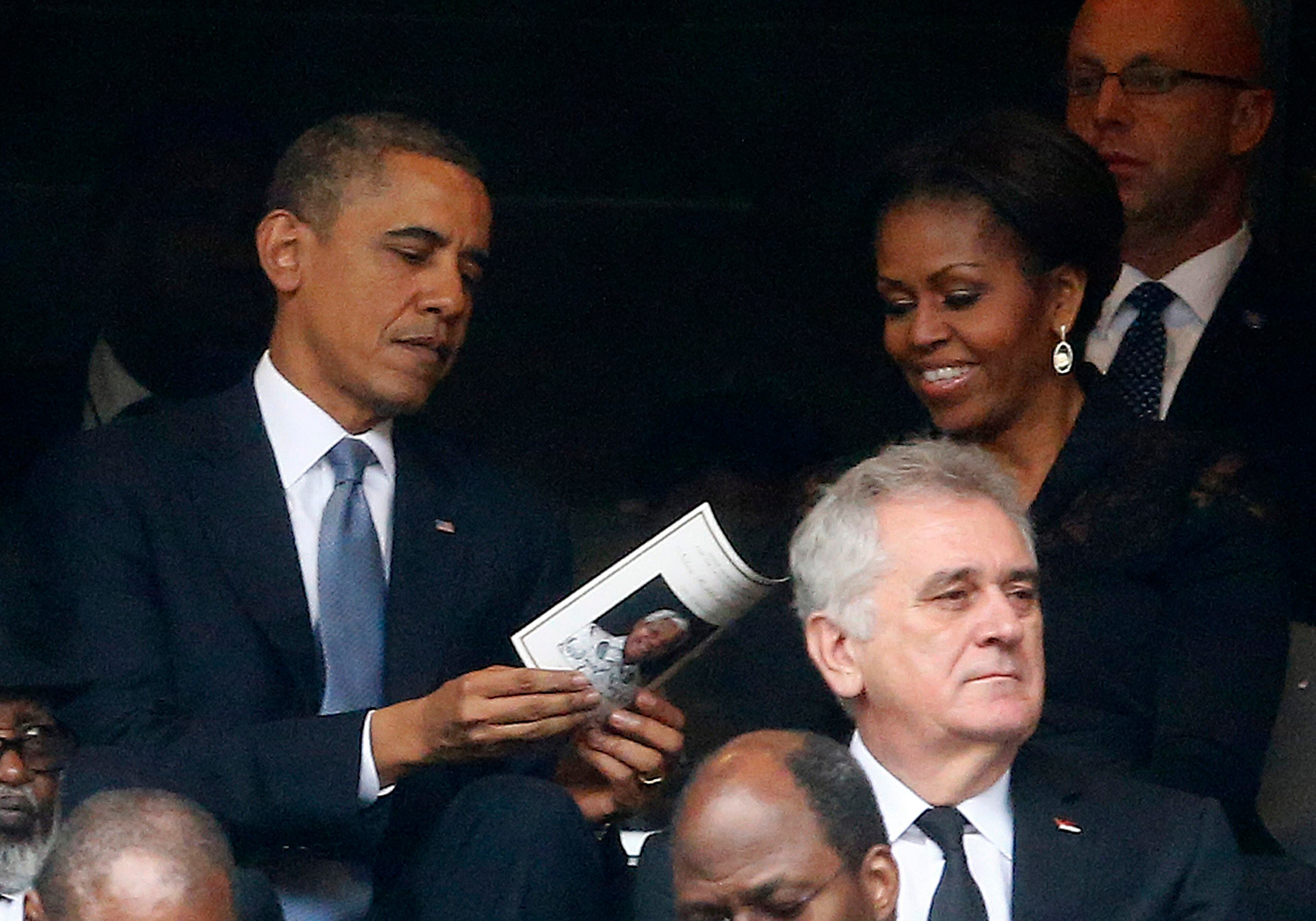 U.S. President Barack Obama (back L) and his wife, first lady Michelle Obama look at the official program booklet during the memorial service for late South African President Nelson Mandela at the First National Bank stadium, also known as Soccer City, in Johannesburg December 10, 2013. World leaders, from Obama to Cuba's Raul Castro, will pay homage to Mandela at the memorial that will recall his gift for bringing enemies together across political and racial divides. REUTERS/Kai Pfaffenbach