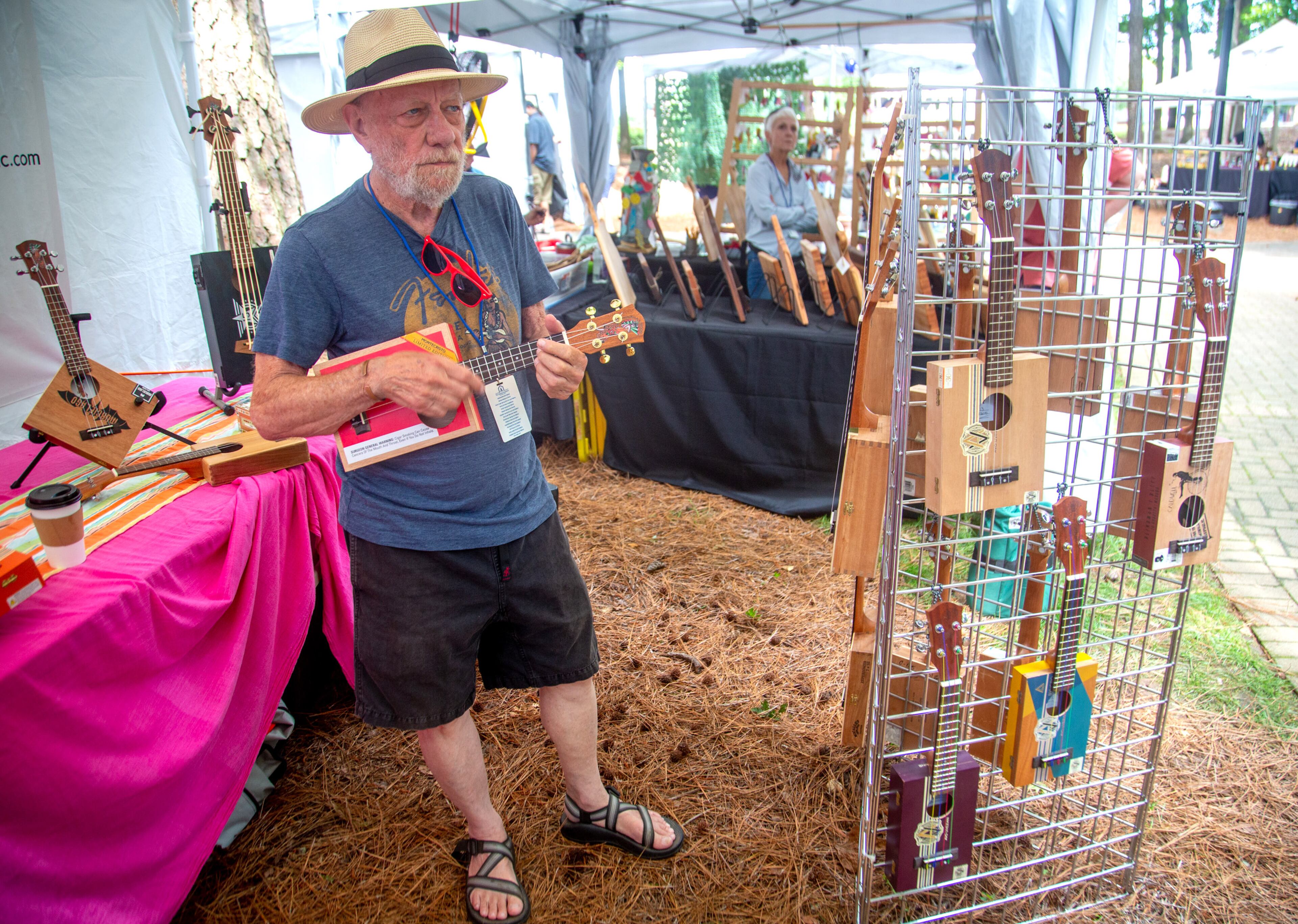 John Kelly plays one of his handcrafted cigar box ukuleles while waiting for customers during the Roswell Spring Arts and Crafts Festival on Sunday, June 13, 2021. (Photo: Steve Schaefer for The Atlanta Journal-Constitution)