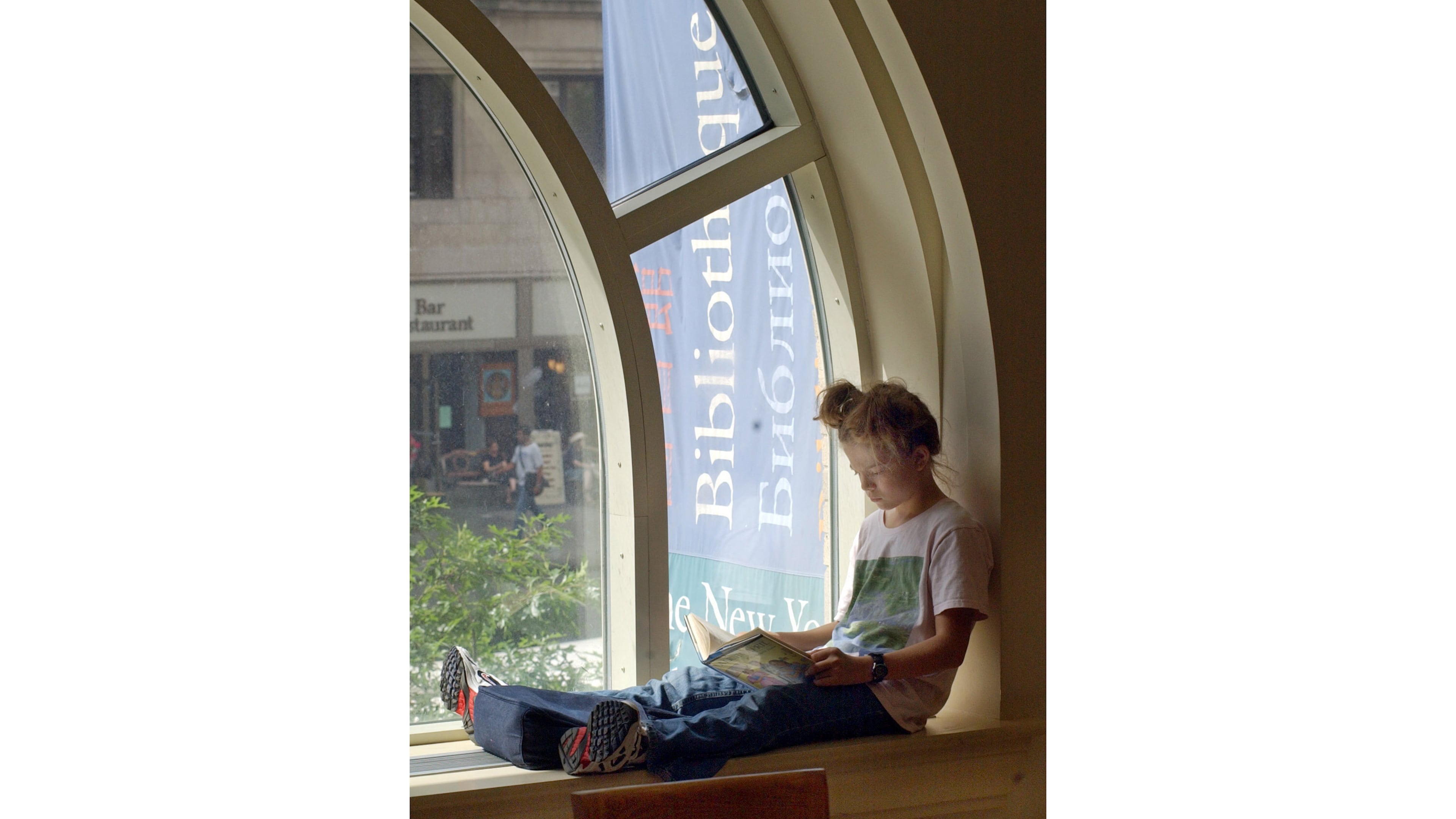 FILE - A young girl reads a book while sitting in a window of the Morningside Heights branch of the New York Public Library on July 29, 2003. (AP Photo/Richard Drew, file)