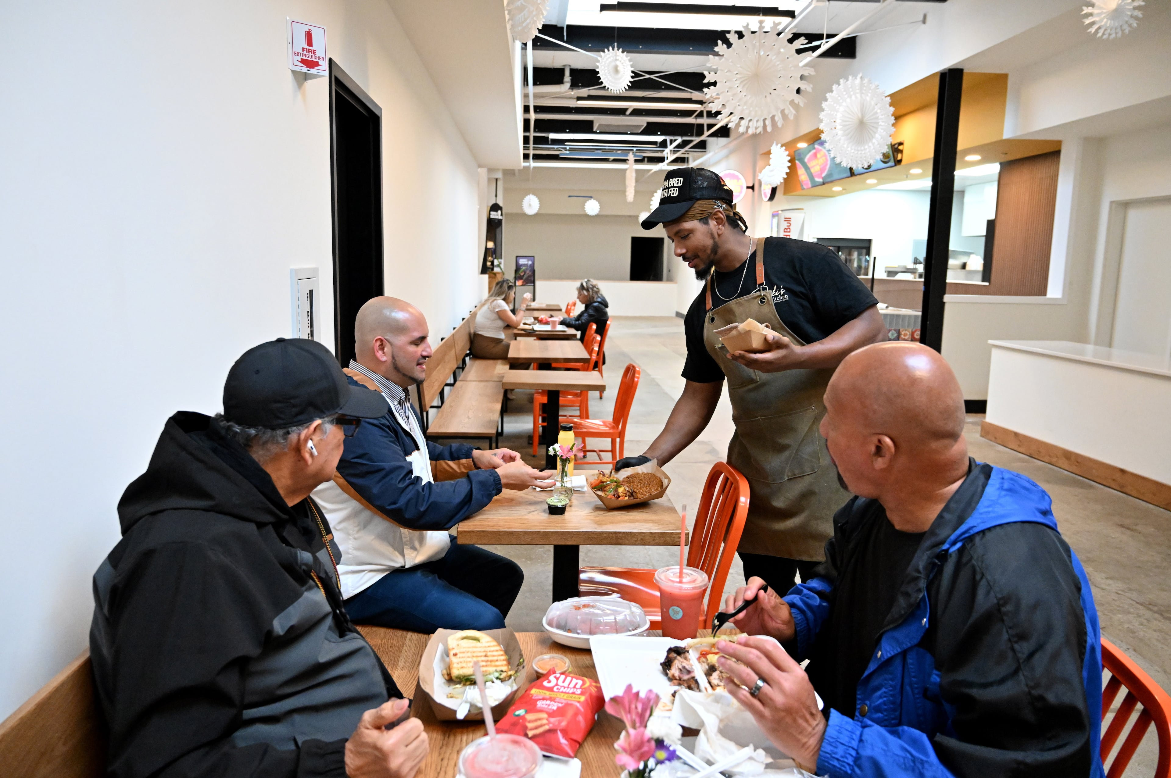 Ali Lemma (right, standing), owner and chef at Ruki’s Kitchen, serves food at Terminal South on Thursday, Feb. 26, 2026, in Atlanta. (Hyosub Shin/AJC)