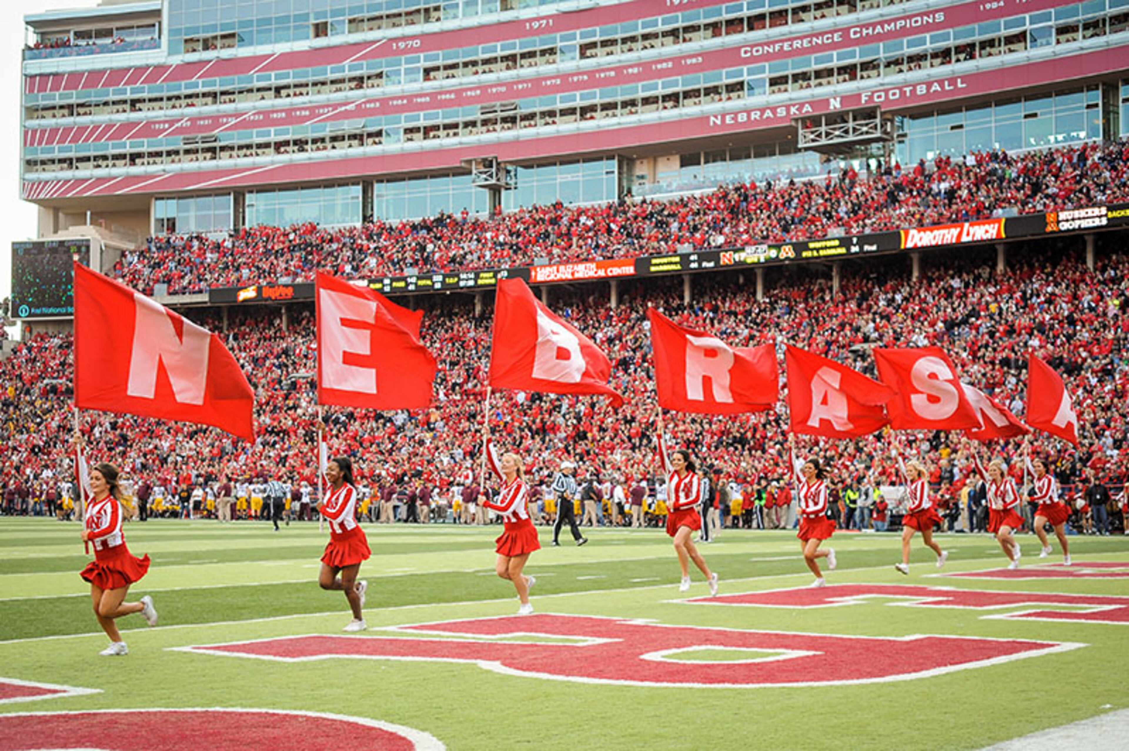 Nebraska Cornhuskers cheerleaders race across the field with flags after the team scored another touchdown against the Minnesota Golden Gophers during their game at Memorial Stadium on Nov. 17, 2012, in Lincoln, Neb.