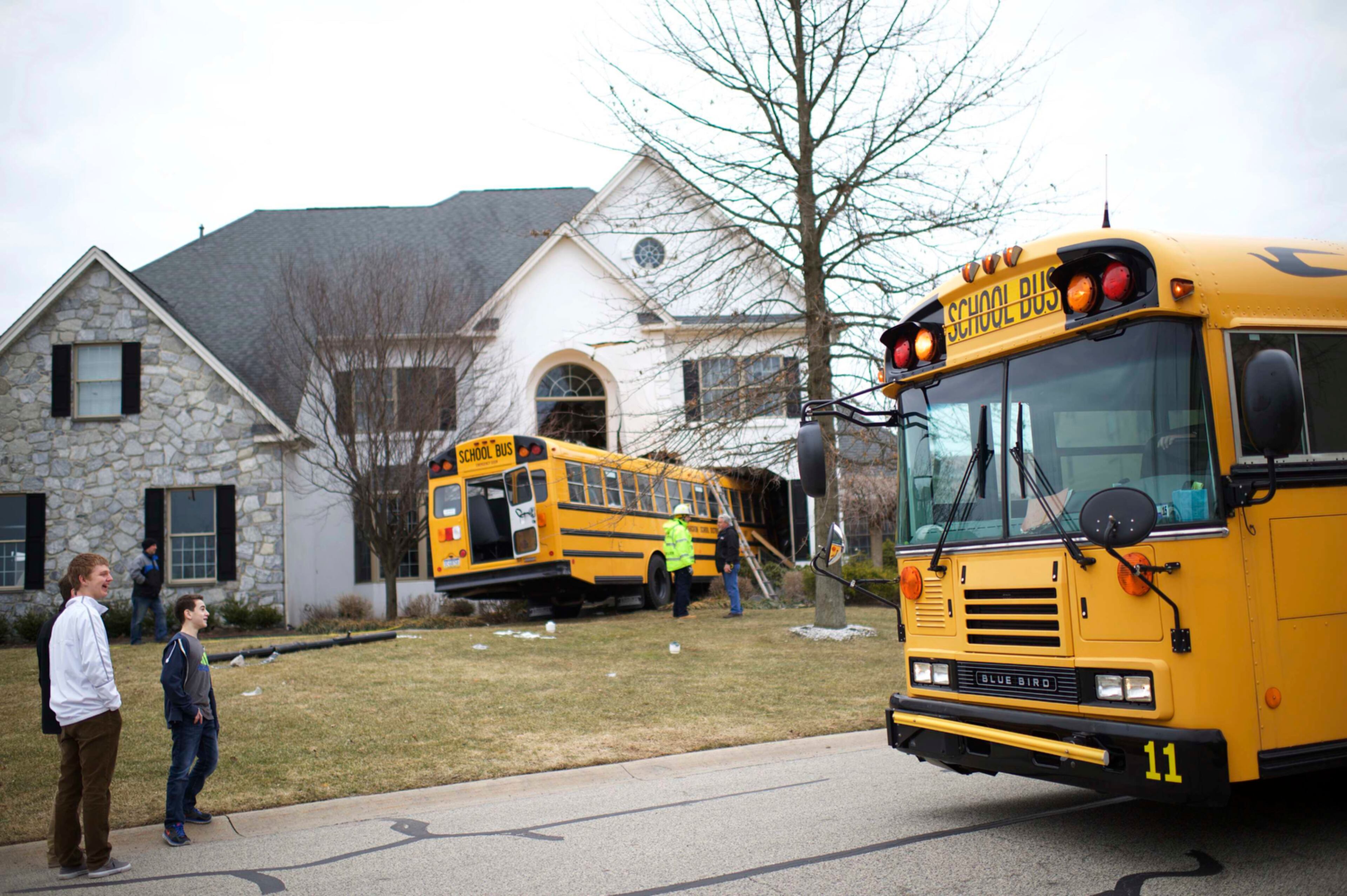 NOT THE NORMAL BUS STOP--A school bus dropping children off from school passes in front of another bus which crashed into a house at the Windermere Development in Blue Bell, Pennsylvania March 24 2015. The school bus carrying nine elementary school students careened off the road and crashed into a occupied home in suburban Philadelphia home on Tuesday, and no injuries were reported, police said. REUTERS/Mark Makela